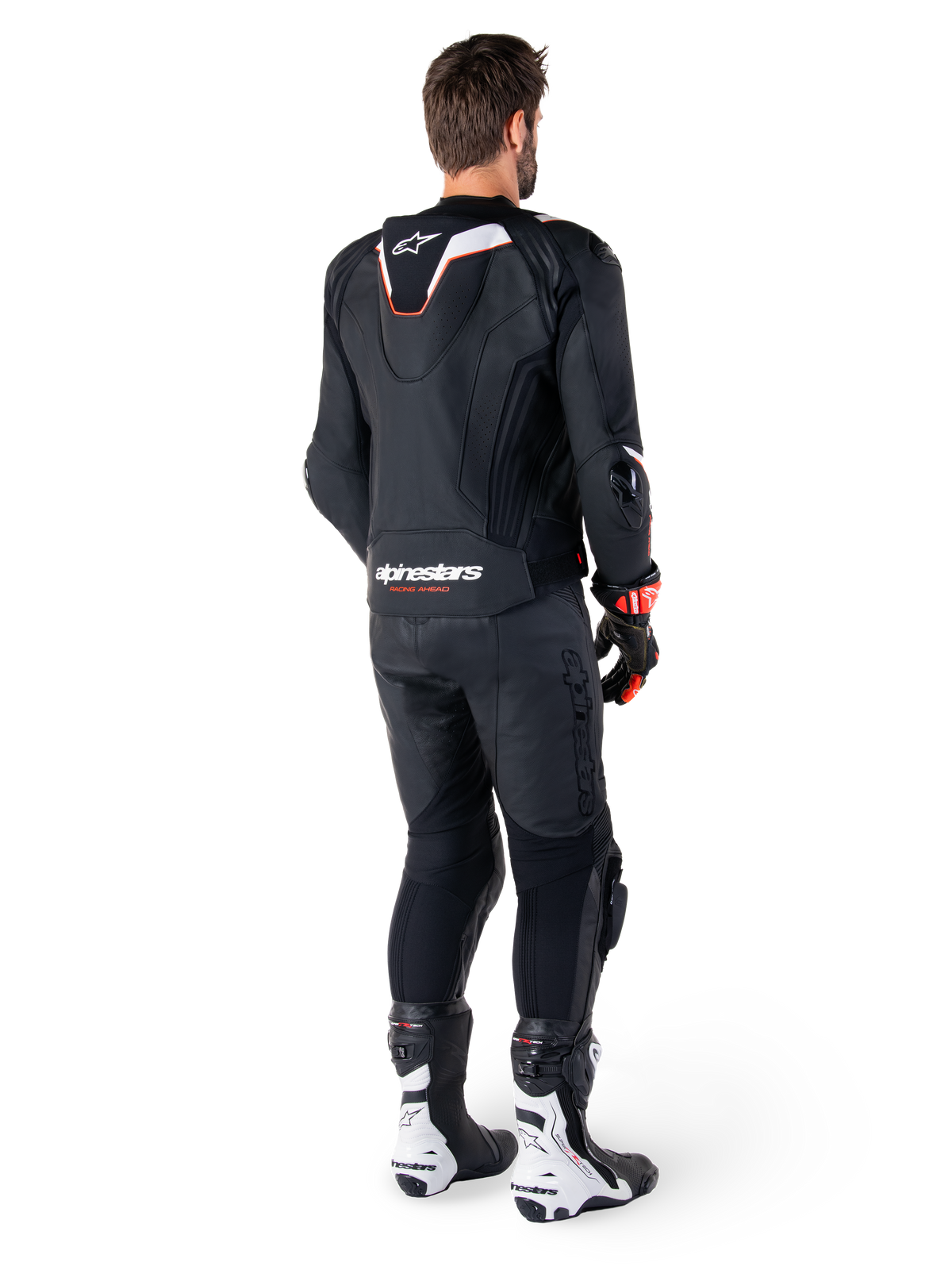 Achteraanzicht van een motorrijder die de Alpinestars Missile V3 Ignition Leren Jas in het zwart draagt, met een slanke sport Aero-hump met witte en rode accenten, Alpinestars-logo op de onderrug, gecombineerd met bijpassende zwarte leren broek en zwart-witte racelaarzen, professionele sportieve rij-outfit