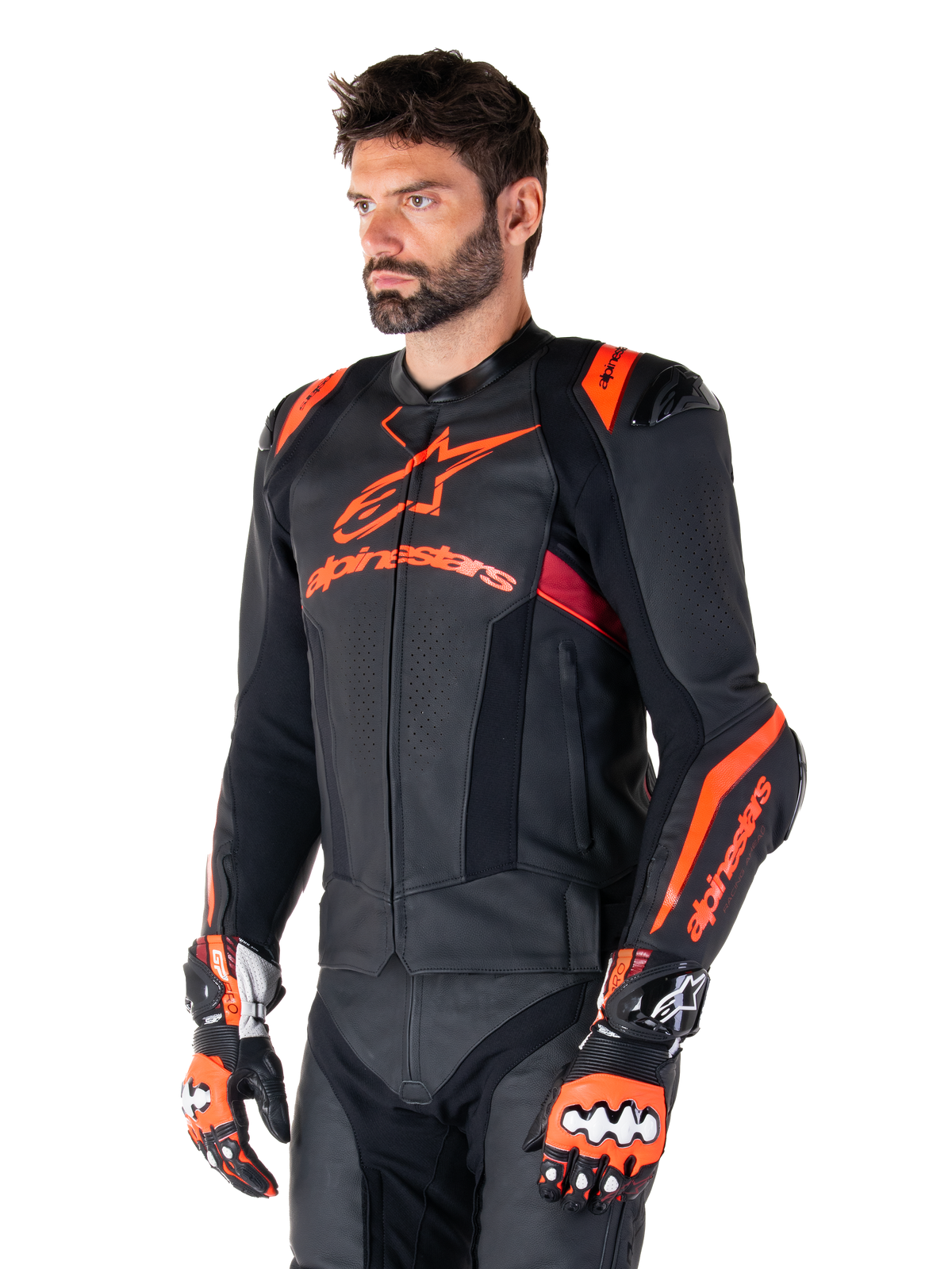 Alpinestars Missile V3 Ignition Leren Jas, zwart met fluo rood en donkerrode accenten, gedragen door een mannelijk model met bijpassende racehandschoenen en leren broek, opvallende Alpinestars-branding, geperforeerde leren panelen en externe schouderprotectoren, professionele motorrace-uitrusting