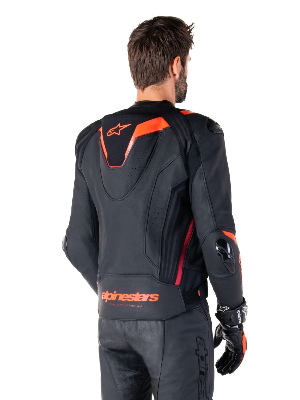 Alpinestars Missile V3 Ignition leren jas, heren race-sportjas, zwart met Red Fluo accenten, achteraanzicht met de slanke aerodynamische sporthump en Alpinestars-branding op de onderrug, gedragen met een zwarte leren broek en racehandschoenen, strak professioneel motorsportontwerp