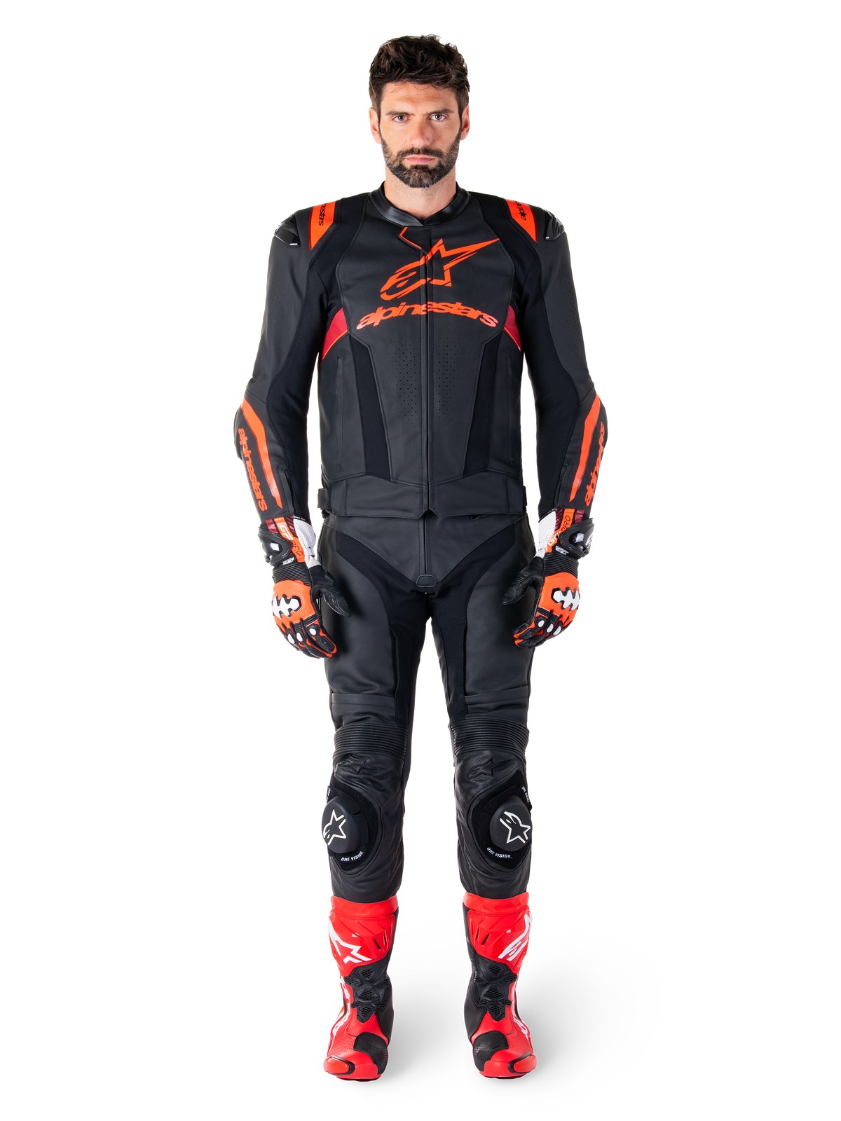 Mannelijk model draagt Alpinestars Missile V3 Ignition leren jas in Black Red Fluo Dark Red, complete motorrace-uitrusting inclusief bijpassende leren broek, racehandschoenen en laarzen, voorzien van opvallende Alpinestars-branding op de borst, naar voren gerichte pose, professionele sport-rijoutfit