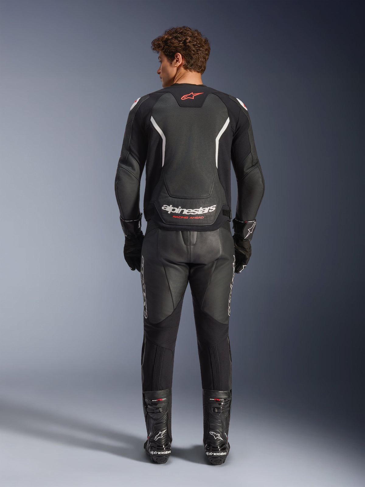 Alpinestars GP Force V2 Air Lederjacke in Schwarz und Weiß, Rückansicht, mit großflächiger Perforation für Luftzirkulation, weißen Schulterakzenten und markantem Branding, getragen mit schwarzer Leder-Motorradhose und Stiefeln