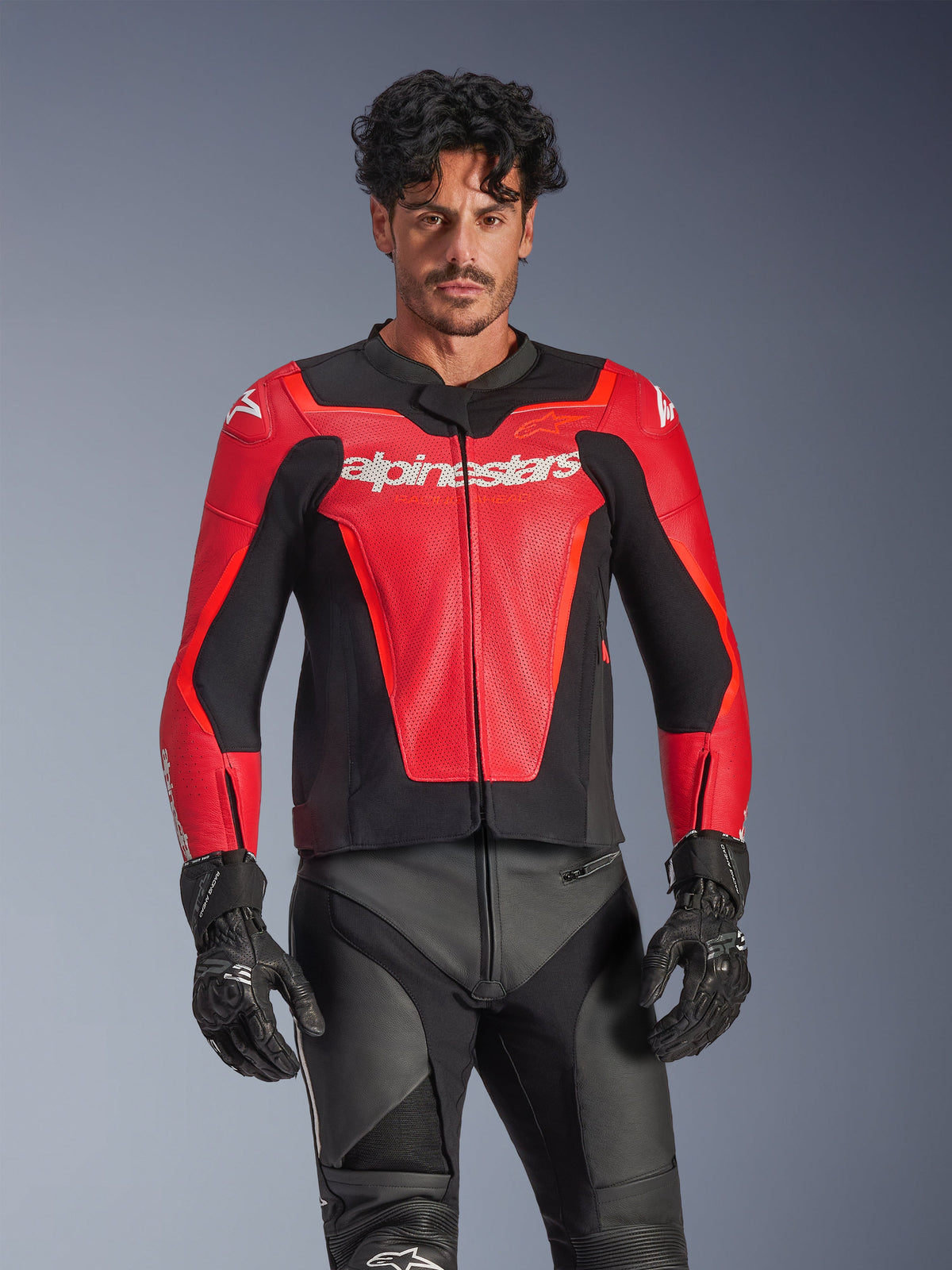 Blouson en cuir Alpinestars GP Force V2 Air, veste de moto de course rouge et noire, conception en cuir perforé avec logo Alpinestars blanc, porté par un mannequin homme et associé à un pantalon de course et des gants noirs