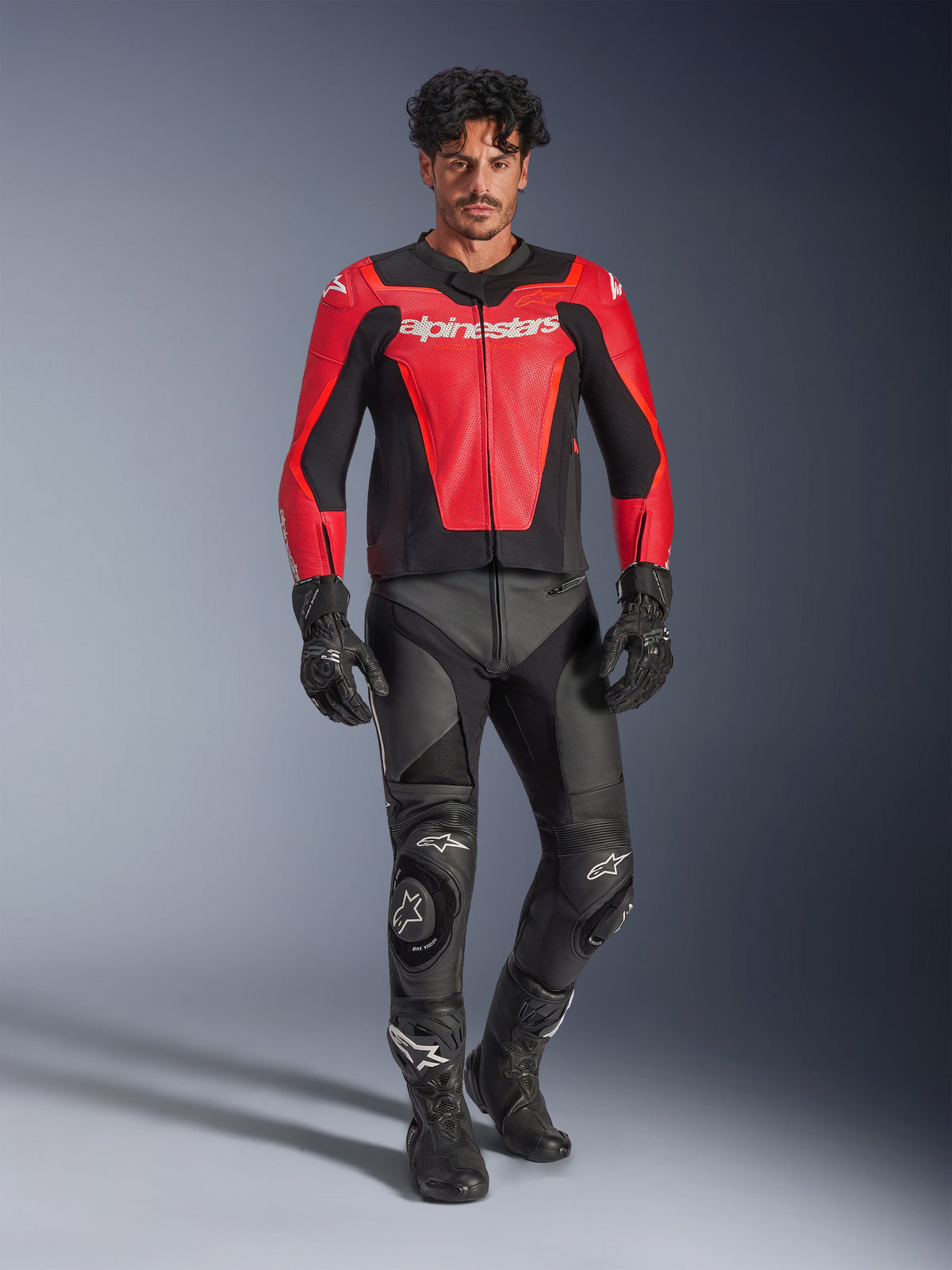 Blouson en cuir Alpinestars GP Force V2 Air, rouge et noir, cuir perforé avec logo blanc, porté par un mannequin avec un pantalon de course et des gants en cuir noir, équipement de moto professionnel
