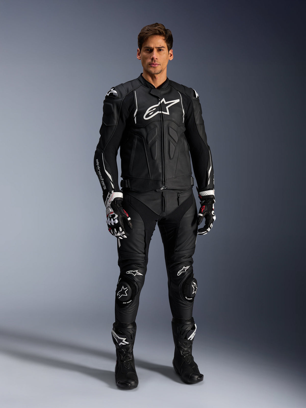Alpinestars Missile V3 Lederhose, Schwarz, getragen von einem männlichen Fahrer als Teil eines kompletten Leder-Motorrad-Rennoutfits, mit weißem Alpinestars-Branding, schützenden Knieschleifern, Rennstiefeln und Handschuhen.
