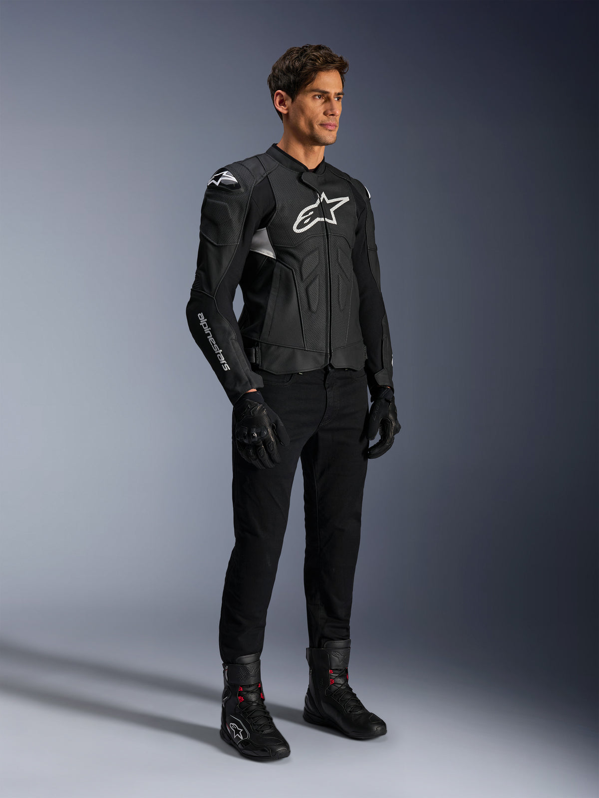 Alpinestars Dusk Airflow Leren Jas, zwart en wit, gedragen met zwarte motorbroek, handschoenen en laarzen, voorzien van geperforeerde leren panelen en witte logo-branding, sportieve road racing stijl.