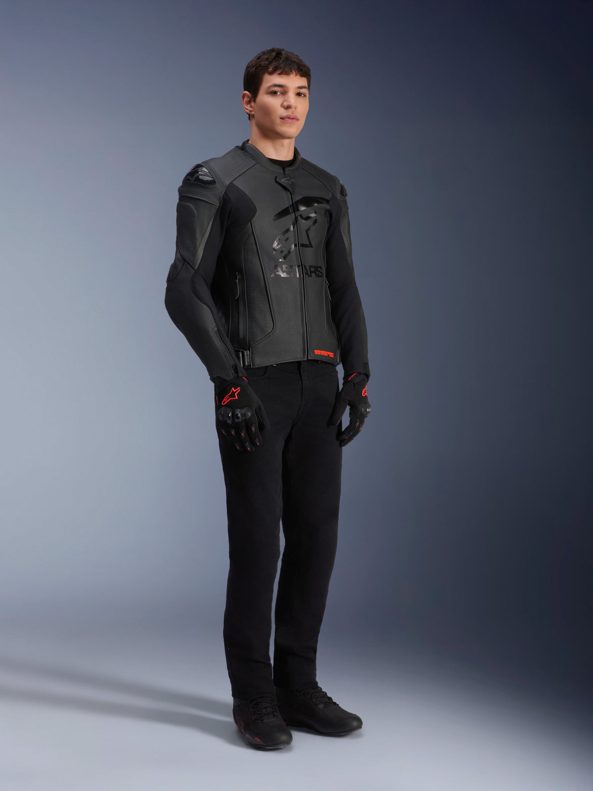 Alpinestars GP Plus R V4 Airflow Lederjacke, Schwarz, getragen von einem männlichen Model mit schwarzer Fahrhose und Handschuhen mit roten Akzenten, mit perforierten Lederpaneelen und integrierten Schulterschleifern, Ganzkörper-Studioaufnahme.