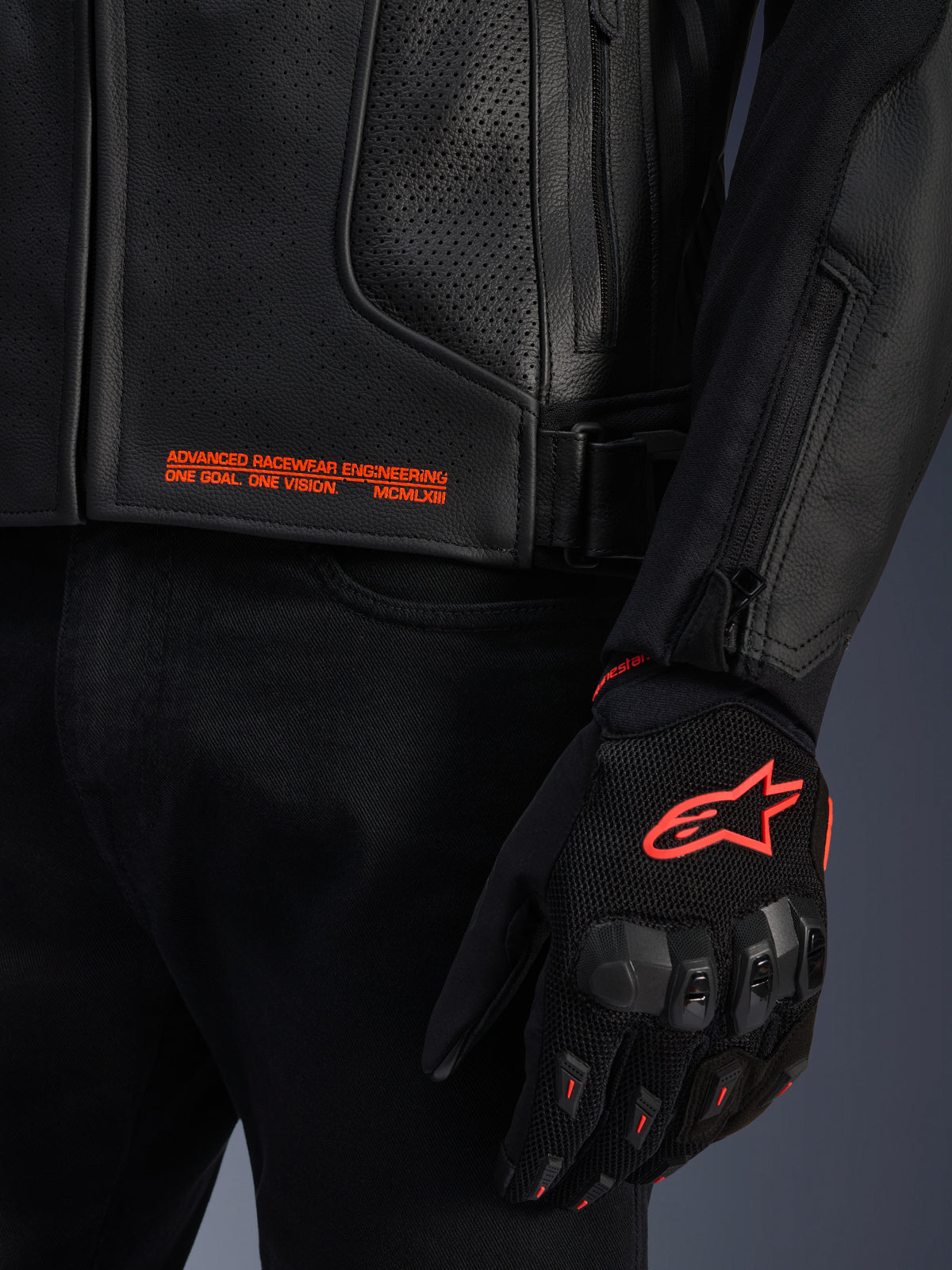 Alpinestars GP Plus R V4 Airflow Leather Jacket, close-up of black perforated leather with orange graphic text, paired with a black and orange motorcycle glove featuring the Astars logo