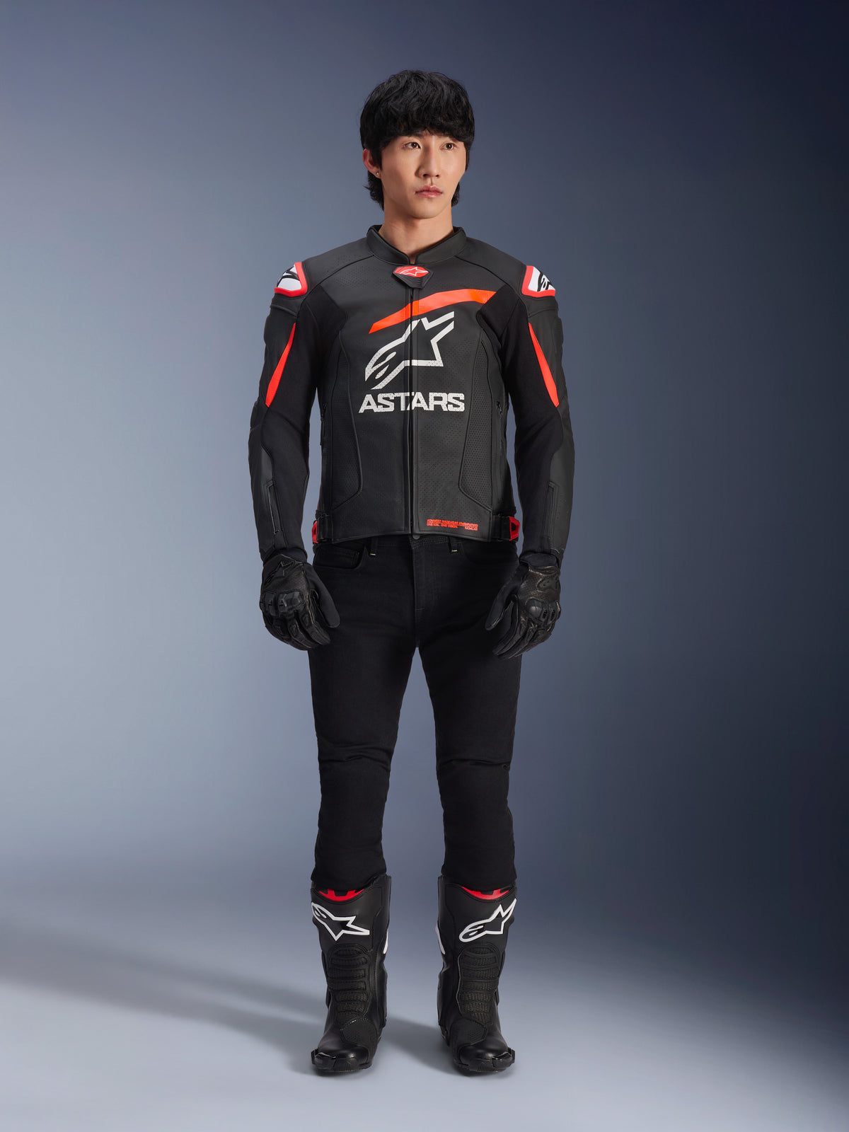 Modèle masculin portant la veste en cuir Alpinestars GP Plus R V4 Airflow, noir avec des accents rouge fluo et blancs, grand logo Astars blanc sur la poitrine, associé à un pantalon technique, des gants et des bottes noirs, équipement de moto haute performance en studio
