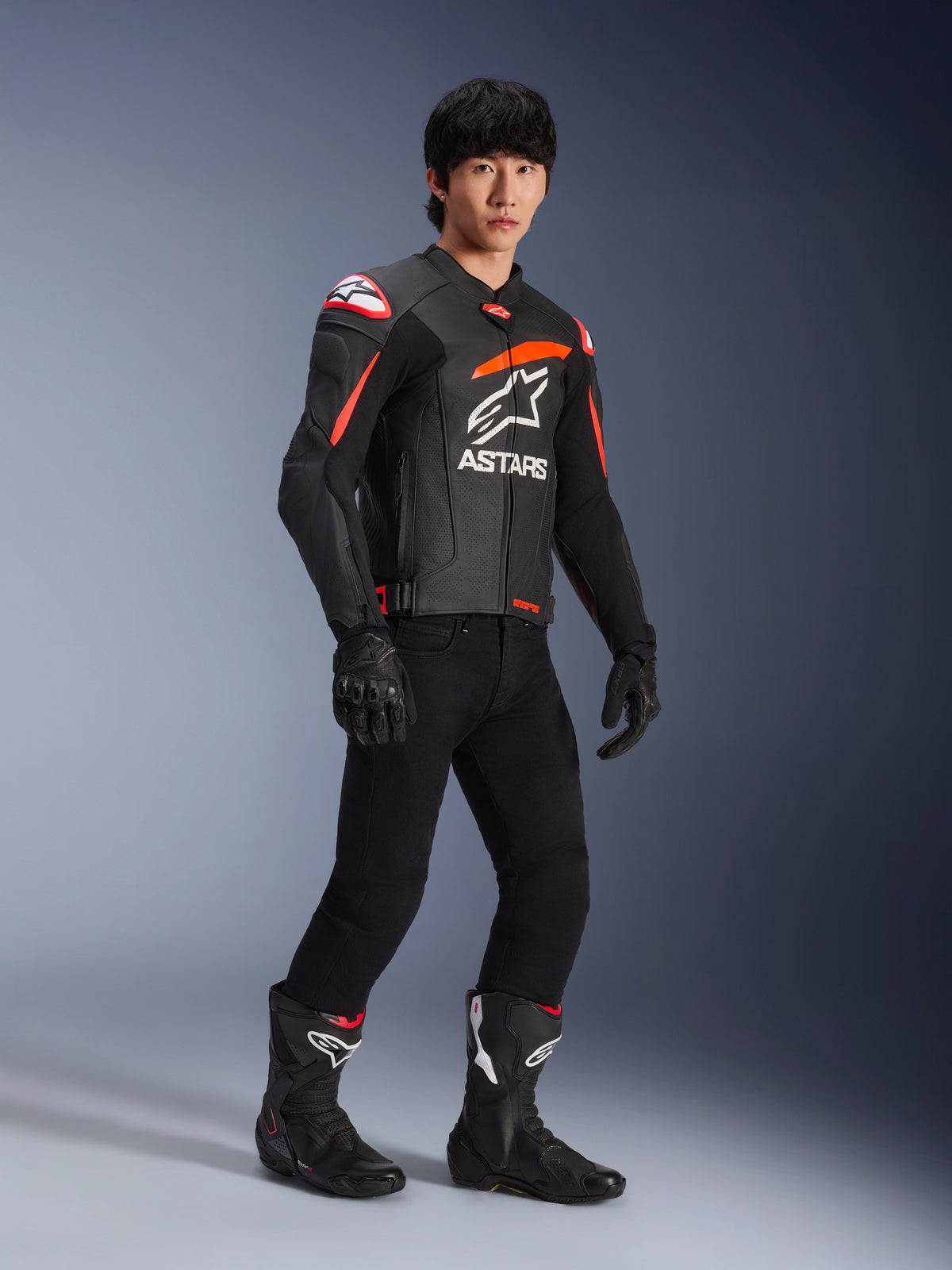 Pilote portant une veste en cuir Alpinestars GP Plus R V4 Airflow, noir avec des accents rouge fluo et blanc, dotée de cuir perforé et du logo ASTARS sur la poitrine, avec pantalon de moto noir et bottes de moto noires, équipement de performance sportive