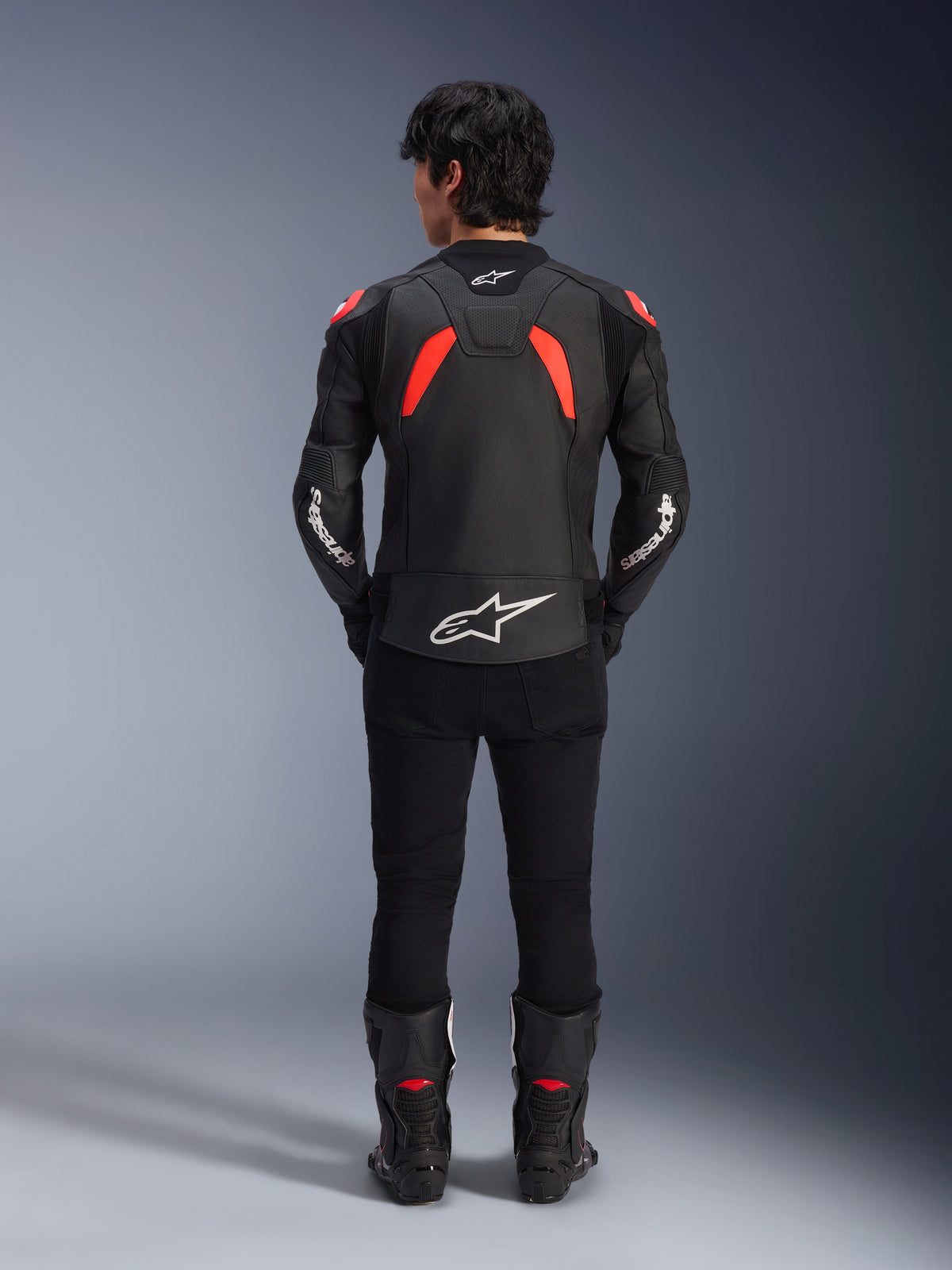 Veste en cuir Alpinestars GP Plus R V4 Airflow, Noir Rouge Fluo et Blanc, vue de dos sur un mannequin, avec des panneaux en cuir perforé et des logos blancs, portée avec un pantalon de moto noir et des bottes