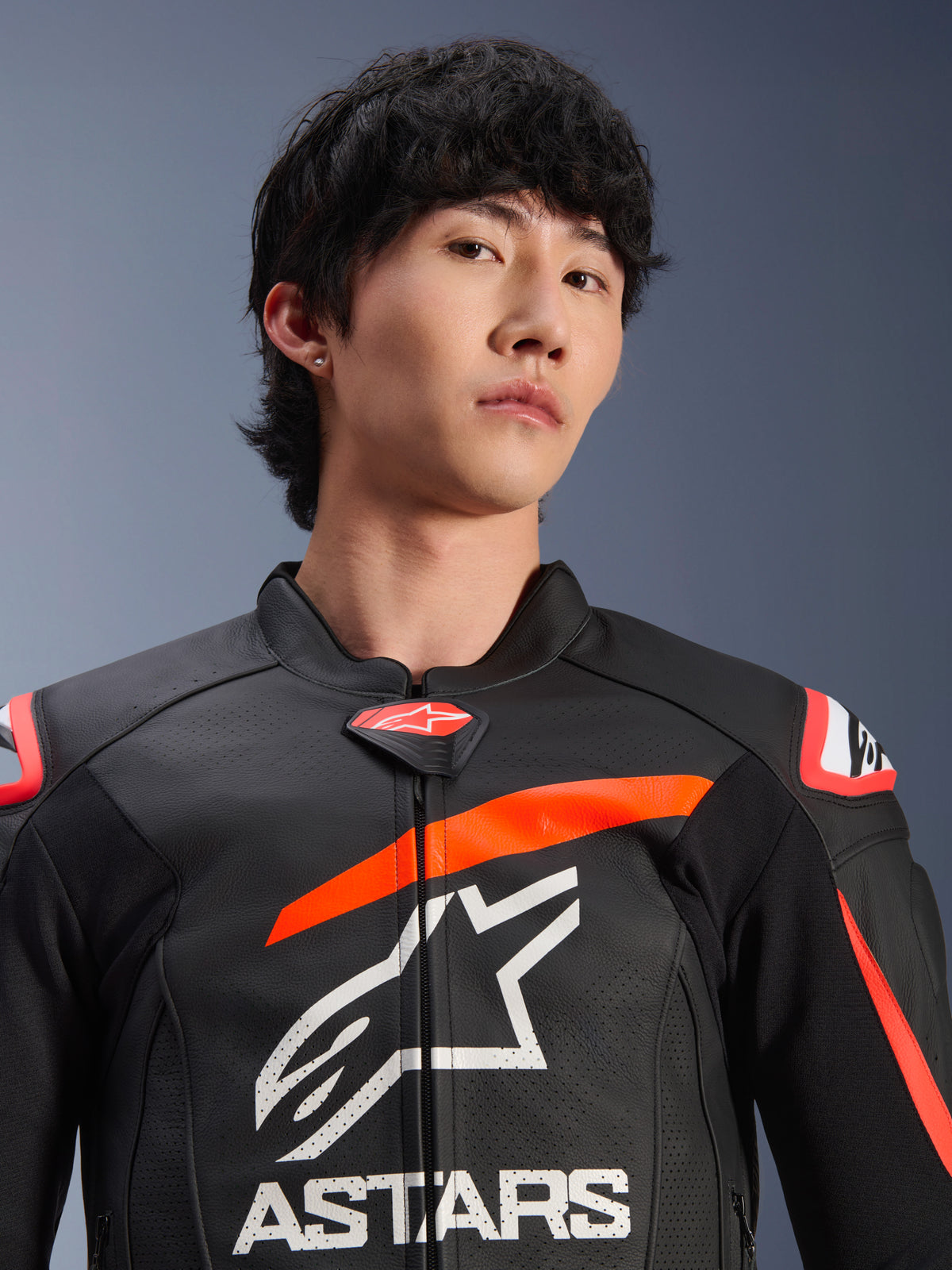 Veste en cuir Alpinestars GP Plus R V4 Airflow, noire avec accents rouge fluo et blancs, portée par un homme, avec un logo Astars blanc et un marquage proéminents sur la poitrine, panneaux en cuir perforé pour la ventilation, design haute performance inspiré de la course.