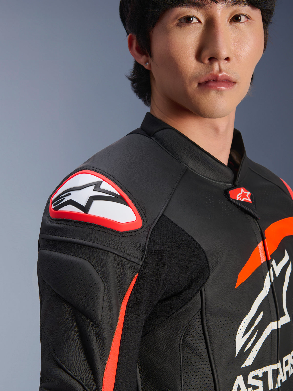 Veste en cuir Alpinestars GP Plus R V4 Airflow, Noir Rouge Fluo Blanc, gros plan du mannequin portant la veste, avec le logo Astar proéminent sur le slider d'épaule et le cuir perforé sur la poitrine pour un flux d'air maximal, vêtement de sport moto professionnel