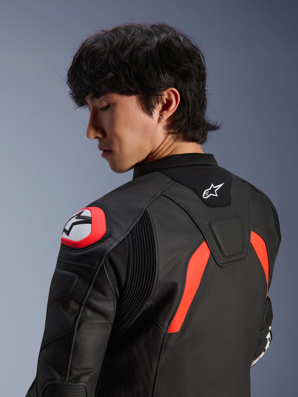 Veste en cuir Alpinestars GP Plus R V4 Airflow, noire avec accents rouge fluo et blanc, vue rapprochée du dos et de l'épaule sur un mannequin, avec zones en cuir perforé, logo Alpinestars et protections d'épaules intégrées pour la performance à moto.