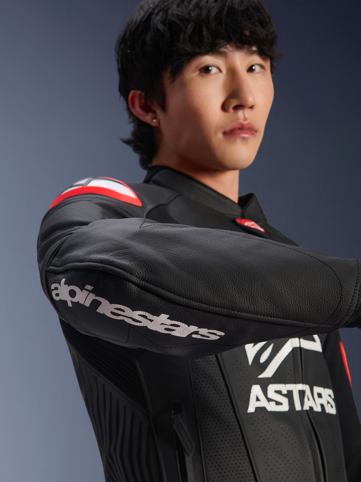 Veste en cuir Alpinestars GP Plus R V4 Airflow, veste de moto, noir rouge fluo blanc, portée par un mannequin, gros plan sur le bras avec logo Alpinestars blanc, détails rouges et blancs sur l'épaule, cuir perforé pour la ventilation, design professionnel inspiré de la course