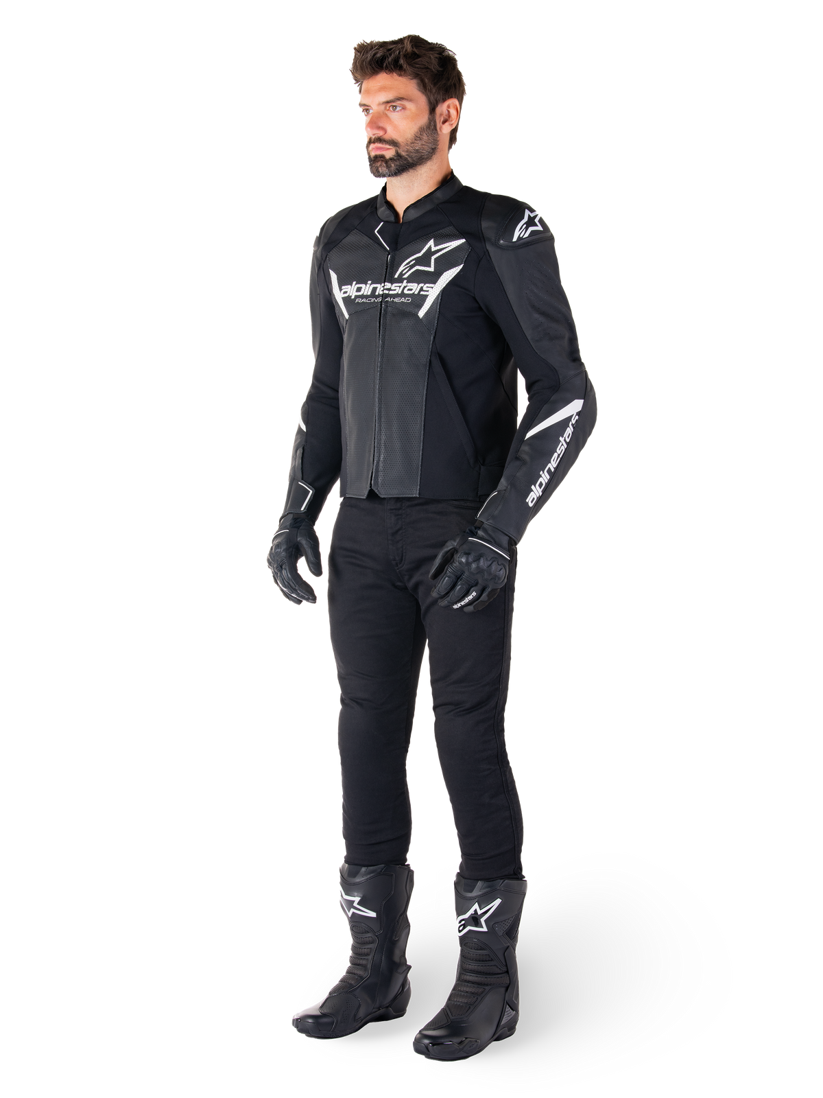 Model draagt Alpinestars Faster V3 Airflow Leren Jas, zwart en wit, voorzien van geperforeerd leer en witte Alpinestars-logo's, gecombineerd met een zwarte motorbroek, handschoenen en laarzen, sportieve motoruitrusting
