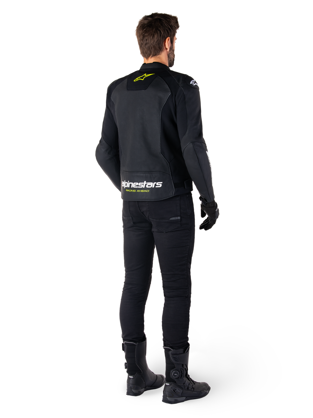 Rückansicht eines Fahrers in der Alpinestars Faster V3 Airflow Lederjacke, Schwarz mit weißen und neongelben Akzenten, kombiniert mit schwarzer Hose und Stiefeln, mit perforiertem Leder zur Belüftung und markantem „RACING AHEAD“-Branding am unteren Rücken.