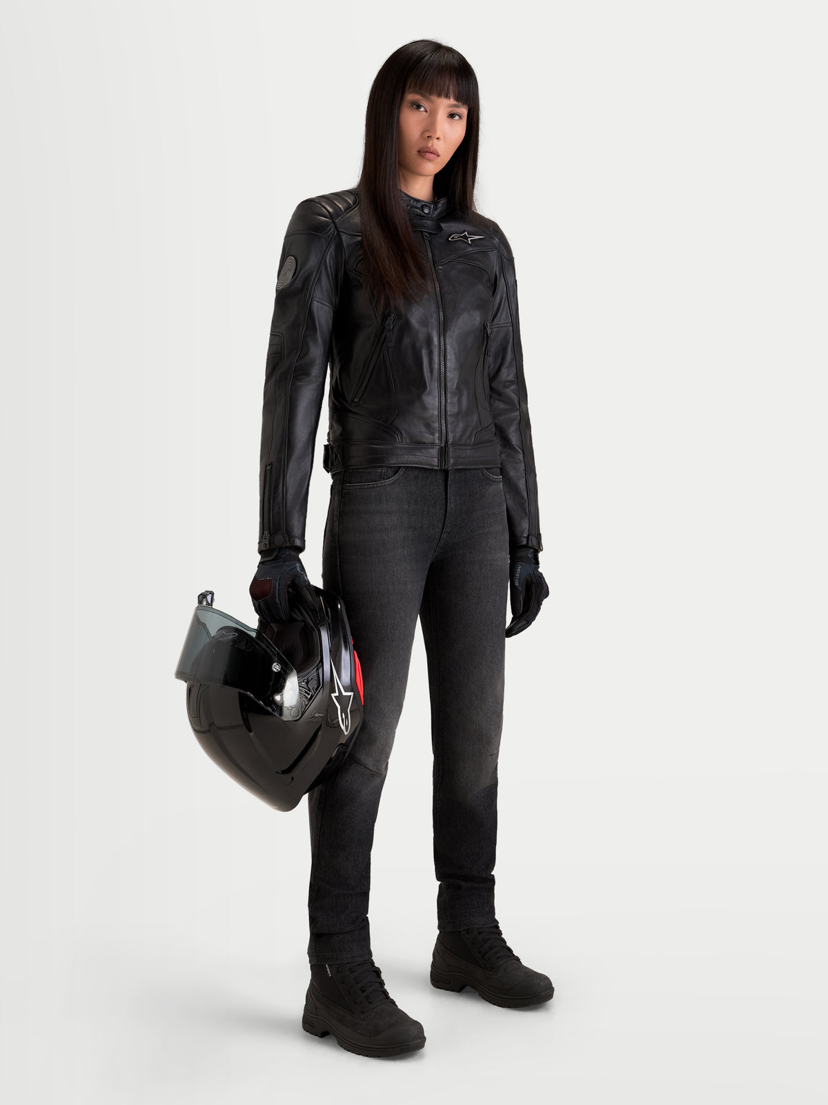 Alpinestars Revea Femme Veste en cuir, blouson de moto urbain contemporain pour femme en cuir noir, porté par un modèle féminin tenant un casque