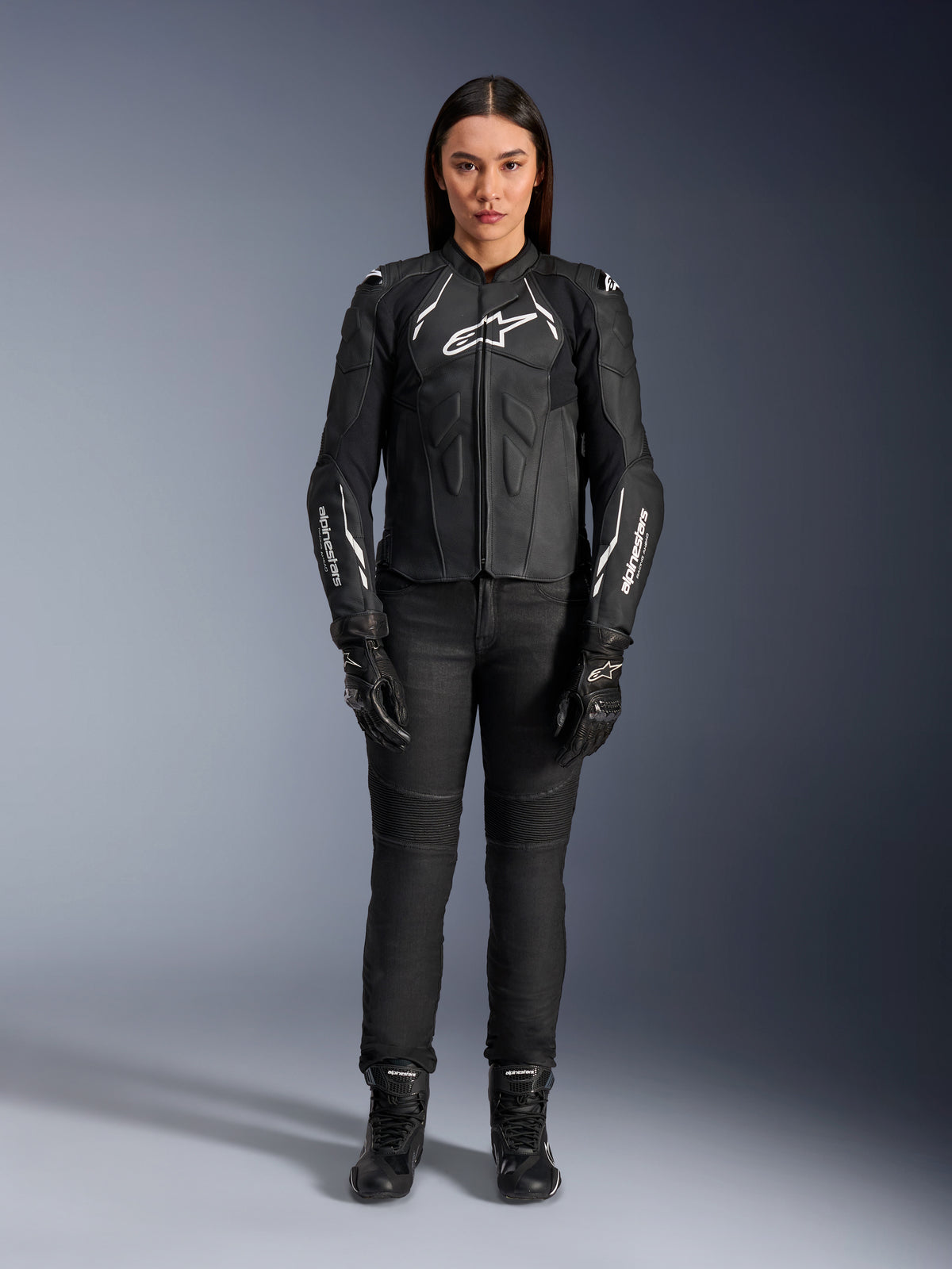 Alpinestars Stella Dusk leren damesjas, zwart en wit, gedragen door een model met bijpassende zwarte broek en laarzen, vooraanzicht, witte Alpinestars logo's op de borst en mouwen, premium runderleren beschermende kleding voor dames
