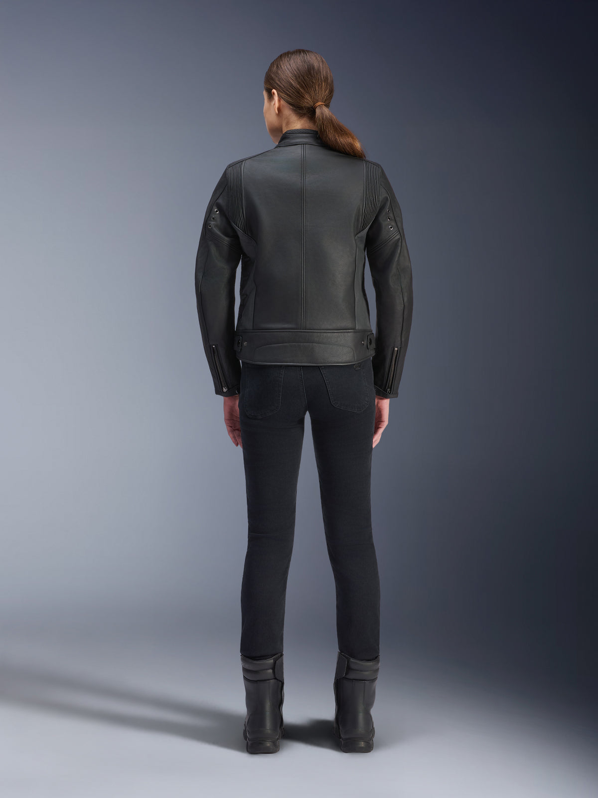 Alpinestars Stella Dyno leren jas, motorjas voor dames, zwart, achteraanzicht met nadruk op de getailleerde runderleren constructie, minimalistisch erfgoedontwerp, gedragen met een zwarte motorbroek en laarzen voor een urban motorlook