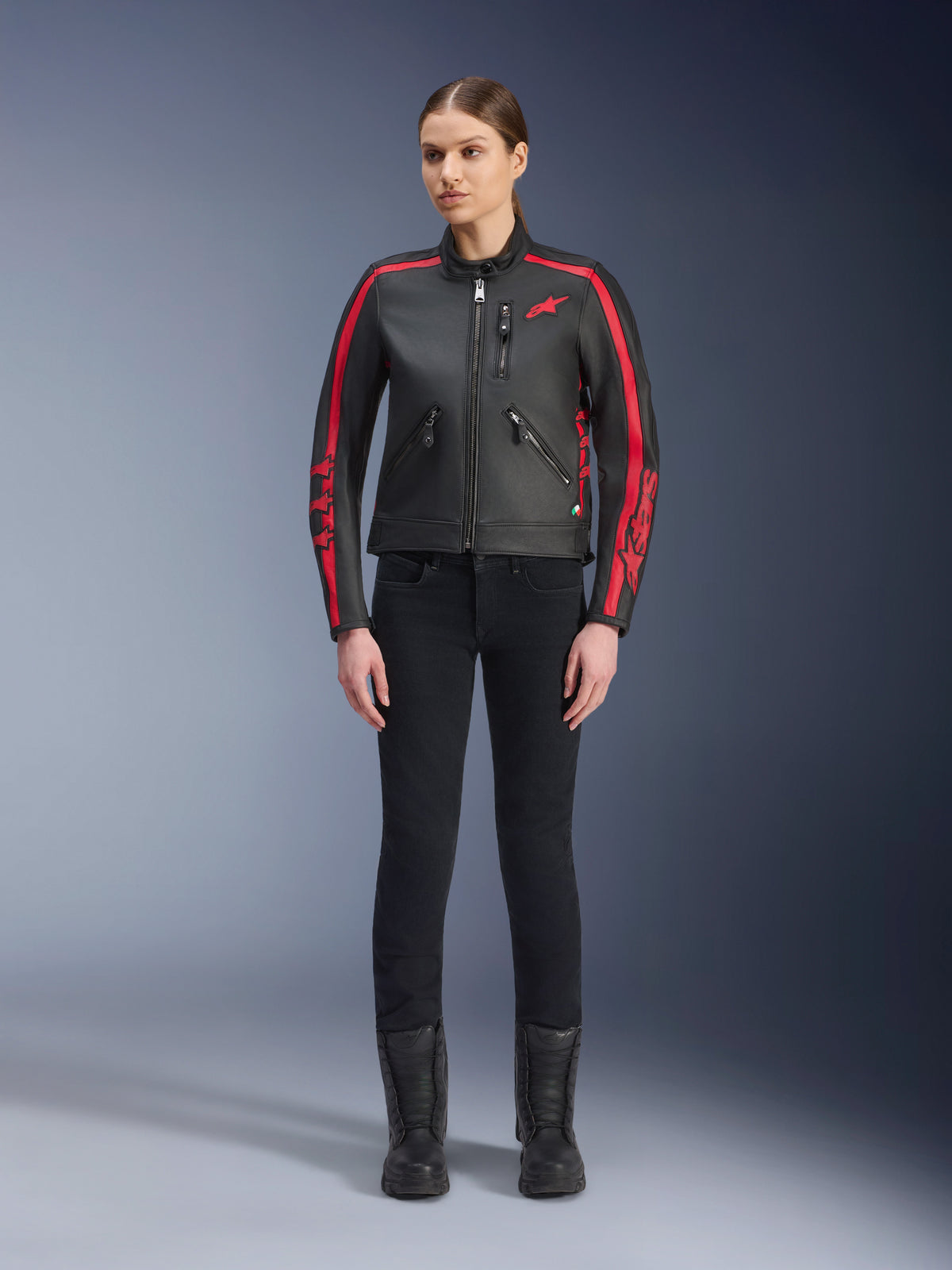 Alpinestars Stella Dyno leren jas, motorjas voor dames, zwart en Haute Red, voorzien van rode racestrepen op de schouders en mouwen, rood ster-logo op de borst, gedragen met een zwarte slim-fit broek en laarzen, premium runderleer met een modern heritage design