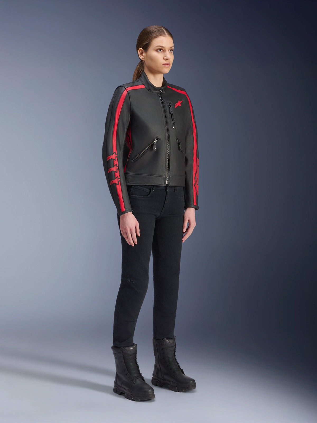 Vrouwelijk model draagt de Alpinestars Stella Dyno Leren Jas in Black Haute Red, gecombineerd met een zwarte broek en laarzen, lederen motorjas in heritage-stijl met rode strepen op de mouwen en een rood logo, urban en road motorkleding voor dames