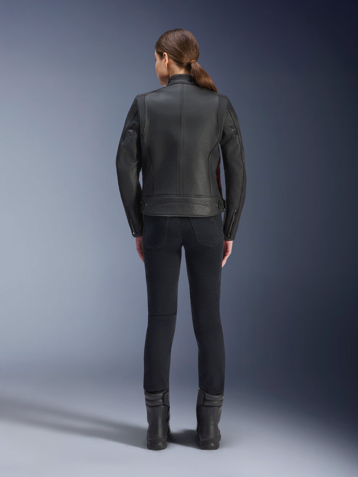 Achteraanzicht van een vrouw die de Alpinestars Stella Dyno leren jas draagt, zwart met Haute Red-accenten, gecombineerd met een zwarte slim-fit broek en zwarte laarzen, modern heritage leren motorjasontwerp.