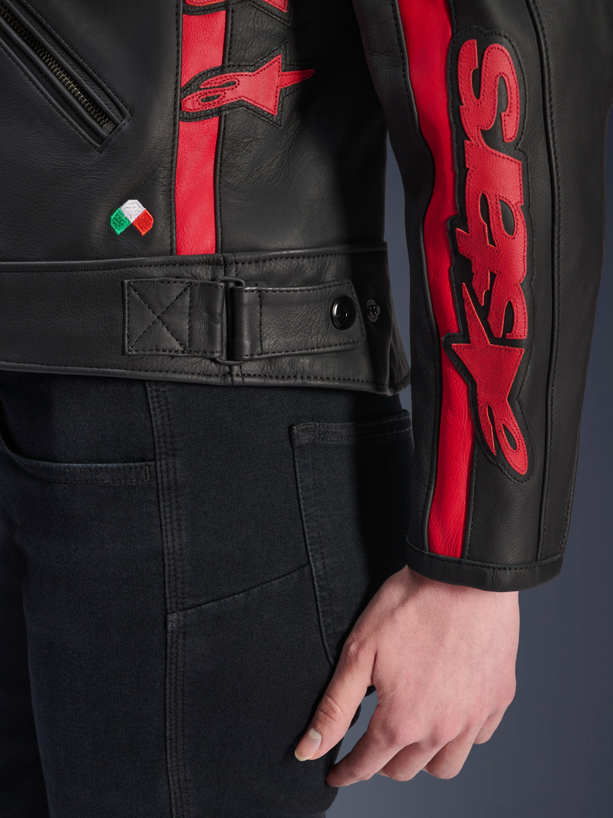 Alpinestars Stella Dyno Leren Jas, dames leren motorjas, Black Haute Red, close-up van de taille en mouw, rode racestrepen met Alpinestars-logo's, verstelbare tailleband, klein borduursel van de Italiaanse vlag, hoogwaardige runderleren constructie