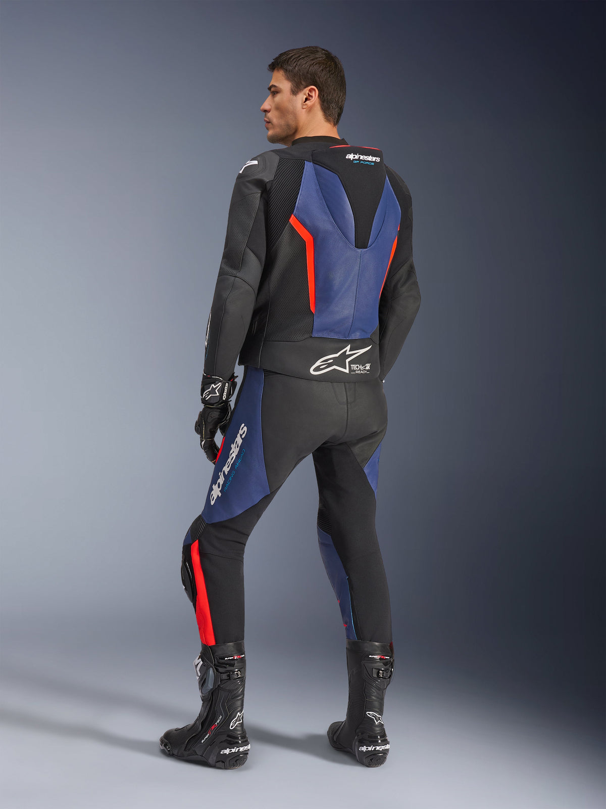GP Force V2 Lederkombi 2-teilig, Schwarz, Blau und Red Fluo, rückseitige Profilansicht an einem Modell, mit aerodynamischem Höcker, perforiertem Leder und Tech-Air Ready-Branding, getragen mit schwarzen Alpinestars Rennstiefeln und Handschuhen