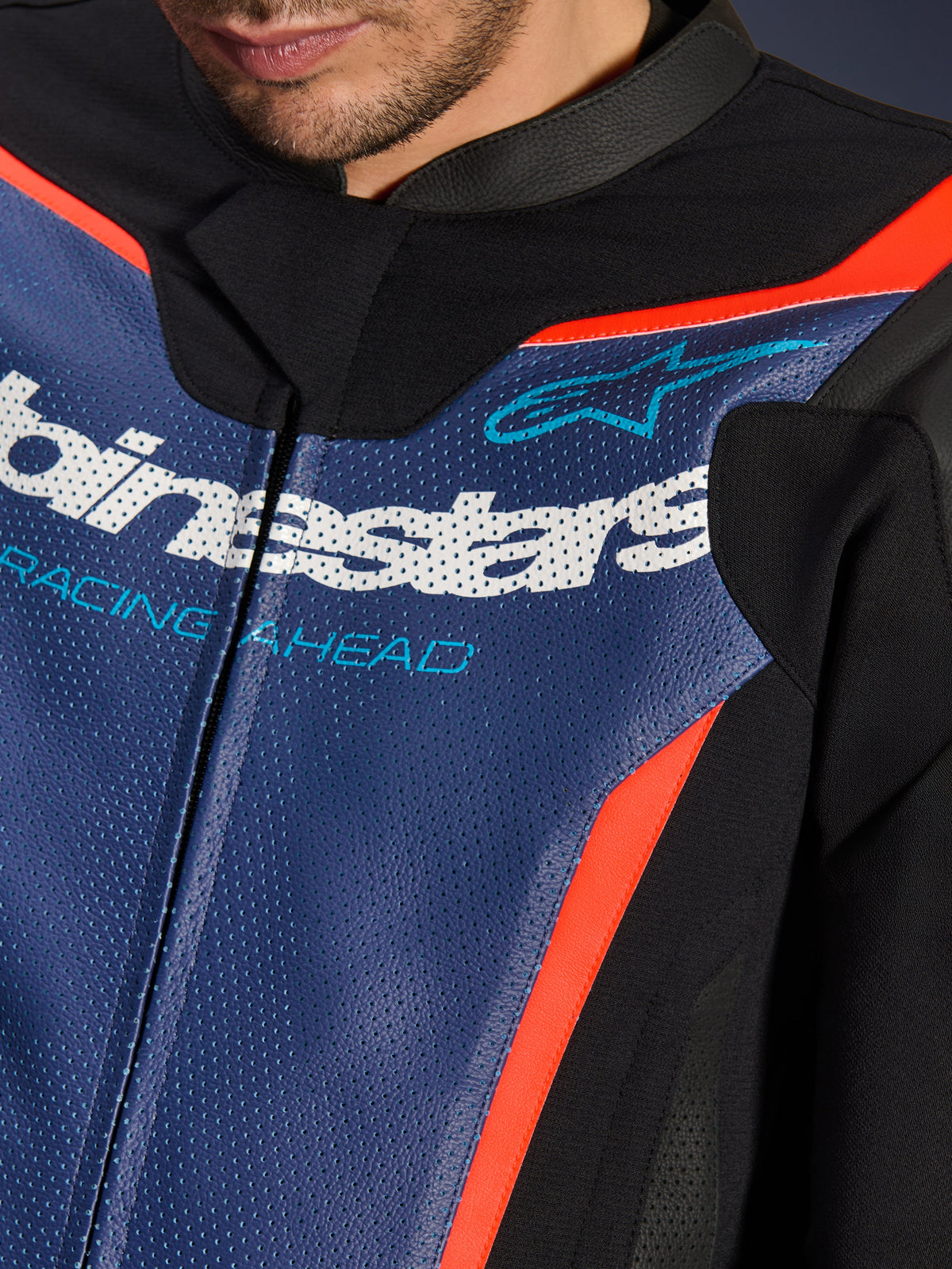 Alpinestars GP Force V2 Lederkombi, 2-teilig, Nahaufnahme des Brustbereichs, perforiertes blaues Leder mit weißem Logo und „RACING AHEAD“-Schriftzug, rote Fluo-Akzente und schwarze Einsätze, professionelle Sport-Fahrausrüstung