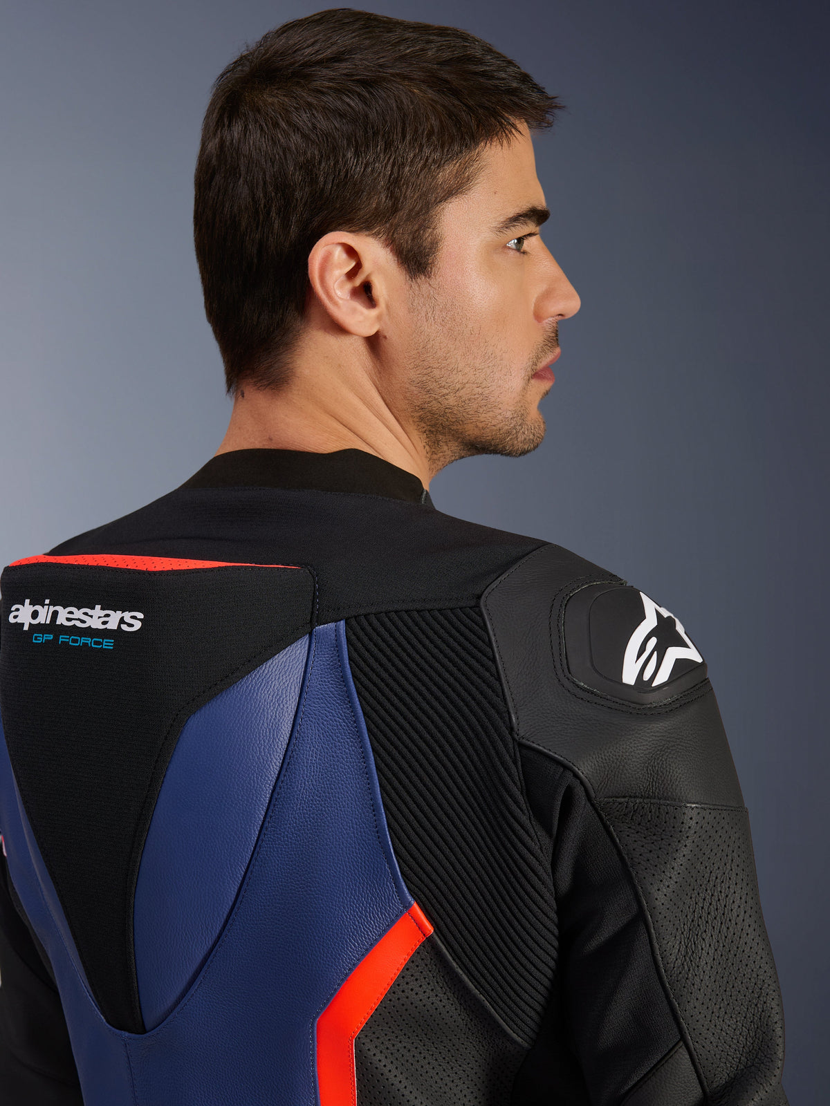 Alpinestars GP Force V2 Lederkombi - 2-teilig, Nahaufnahme des oberen Rückens und der Schulter, aerodynamischer Speed-Hump mit GP Force Logo, DFS Schulter-Slider, Rindsleder in Schwarz, Blau und Fluo-Rot, perforierte Einsätze und Akkordeon-Stretchzonen, professionelle Rennausrüstung