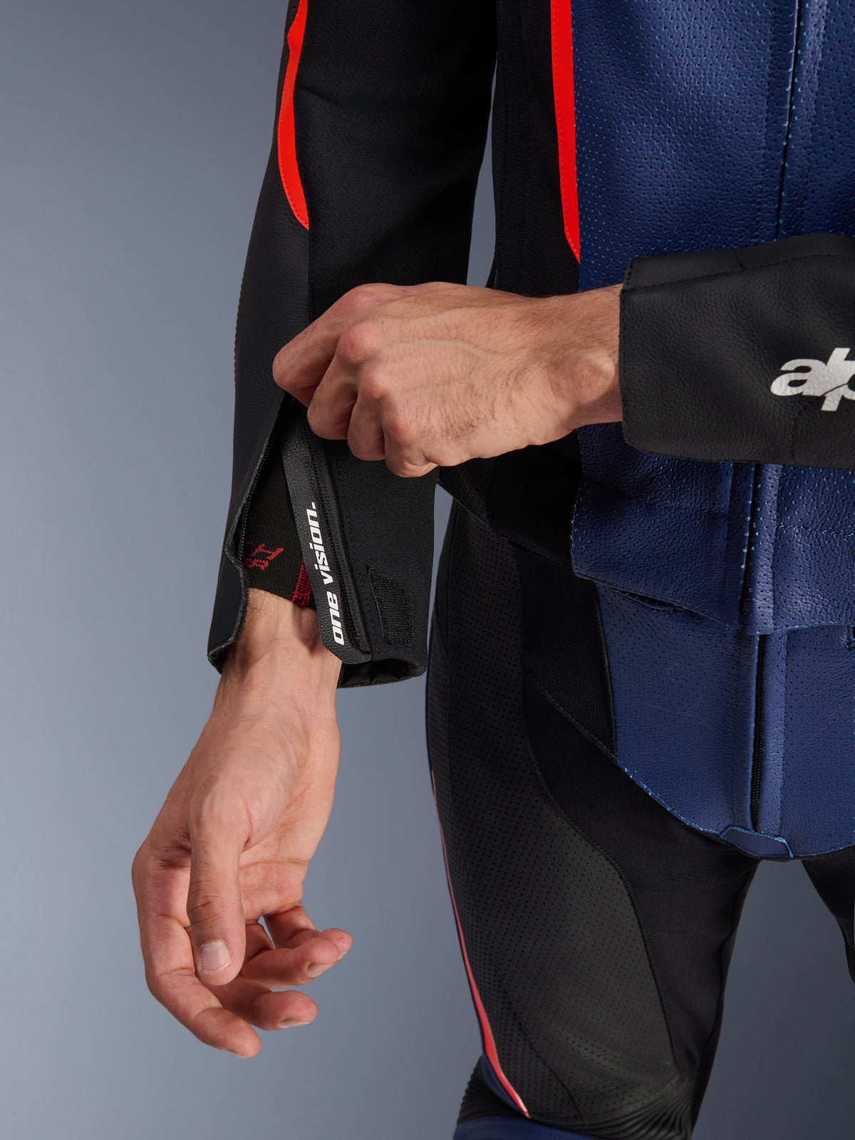 Alpinestars GP Force V2 Lederkombi 2-teilig, Nahaufnahme des Ärmelbündchens und Torsos, Schwarz, Blau und Fluo-Rot, mit perforiertem Leder, Handgelenk-Reißverschluss mit „one vision“-Branding und fluoreszierenden roten Akzenten, professionelle Sport-Fahrerausrüstung