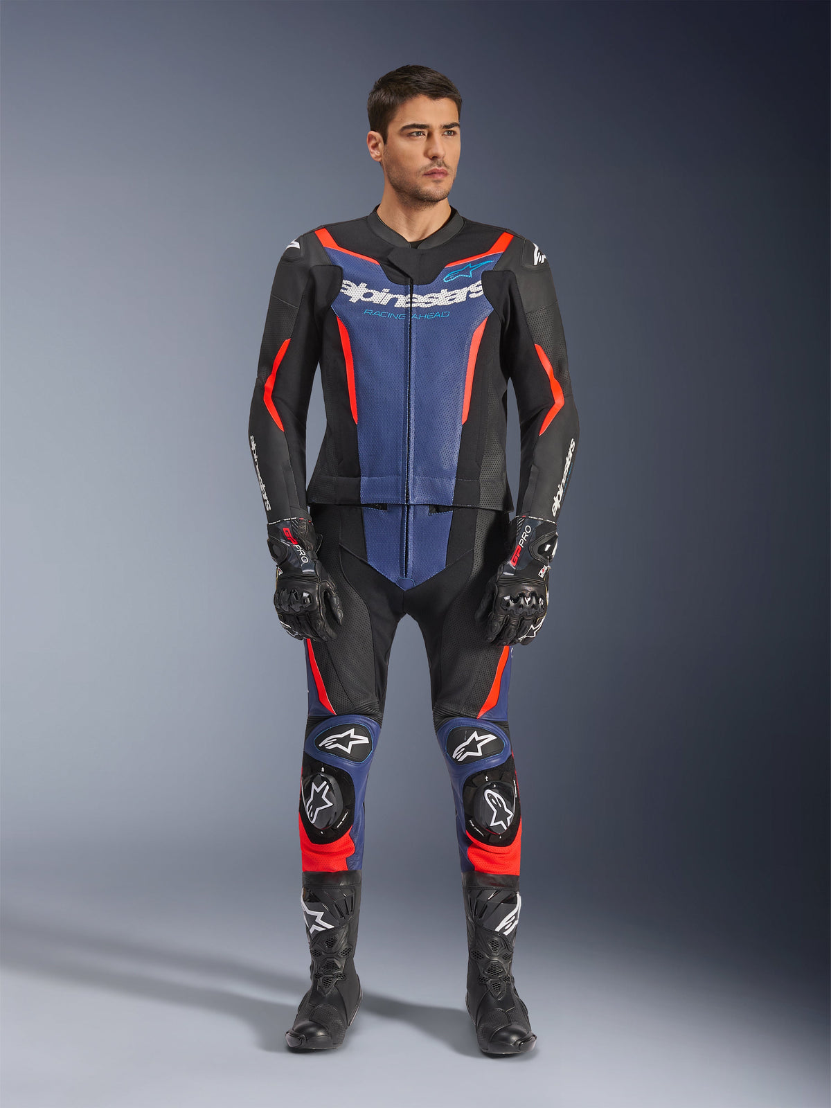 Alpinestars GP Force V2 Lederkombi 2-teilig in Schwarz, Blau und Red Fluo, mit blauen Einsätzen an Brust und Unterschenkeln sowie leuchtend roten fluoreszierenden Akzenten, getragen von einem männlichen Model mit schwarzen Rennstiefeln und Handschuhen, professionelle Motorsport-Schutzkleidung