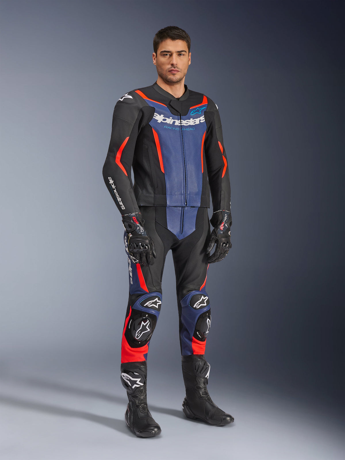 Alpinestars GP Force V2 Lederkombi 2-teilig, Motorrad-Lederkombi, Schwarz, Blau und Neonrot, getragen mit passenden schwarzen Rennhandschuhen und Stiefeln, mit perforierten Einsätzen und Schutz-Slidern, aerodynamisches Design für sportliches Fahren