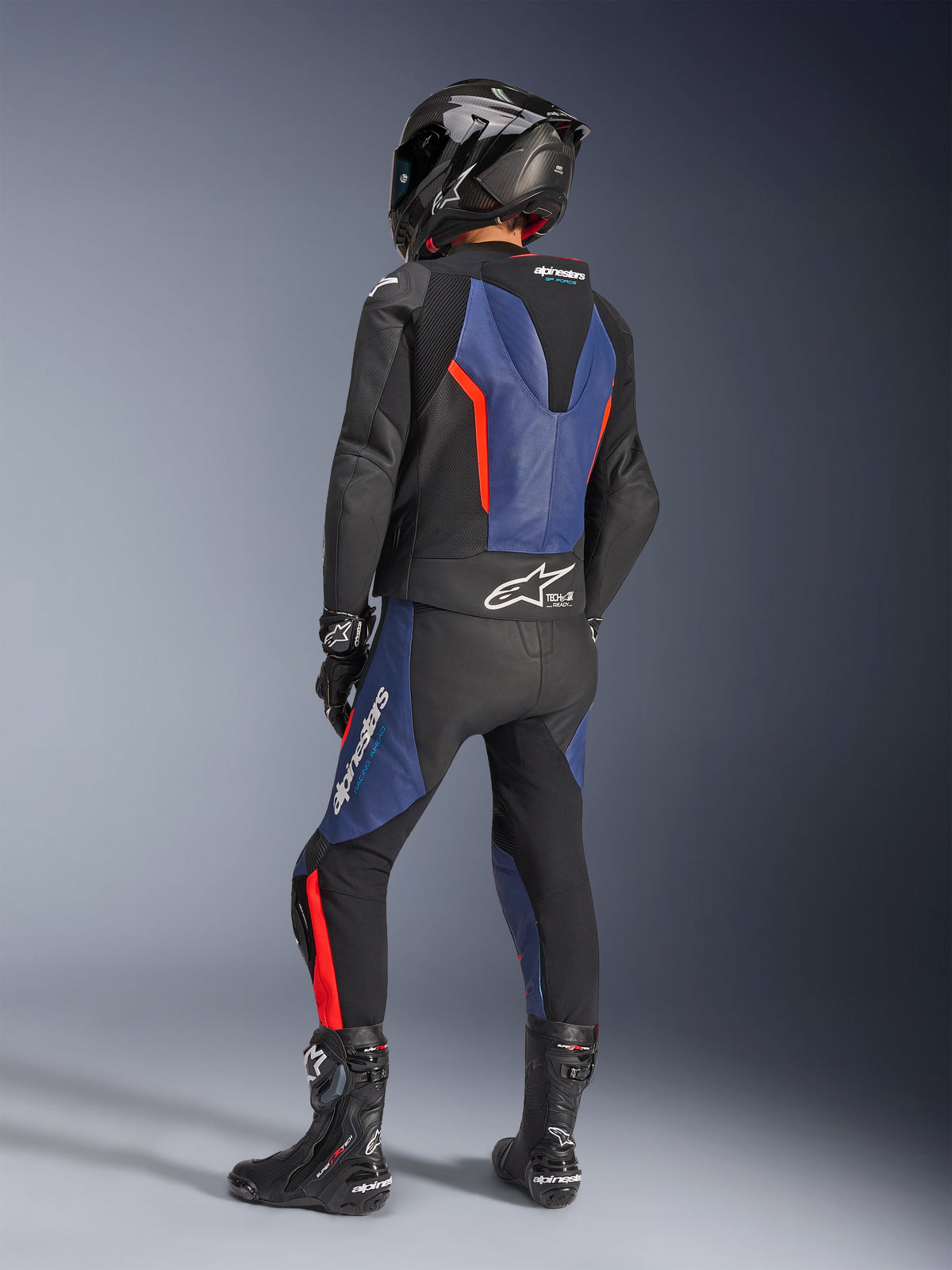 Alpinestars GP Force V2 Lederkombi 2-teilig, Schwarz Blau Rot Fluo, Rückansicht eines Fahrers in professioneller Rennausrüstung, mit integriertem aerodynamischem Höcker und Tech-Air Ready Branding, blaue und rote Fluo-Akzente auf schwarzem Leder, kombiniert mit einem Carbon-Helm und schwarzen Stiefeln, Hochleistungs-Motorradbekleidung