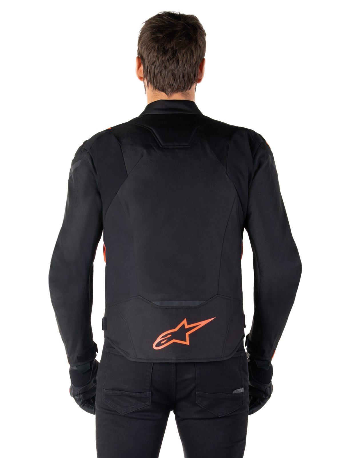 Veste imperméable Alpinestars T-Jaws V4, vue arrière, noir et rouge fluo, arborant un logo Alpinestars rouge en bas du dos, construction en textile technique, portée avec un pantalon et des gants noirs pour un look de pilotage sportif complet