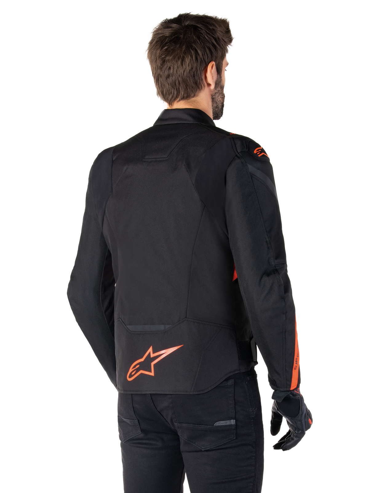 Modèle masculin portant la veste imperméable Alpinestars T-Jaws V4 vue de dos, noir avec des accents rouge fluo, présentant un logo rouge fluo au bas du dos et des détails sur les épaules et les manches, équipement de moto sportif.