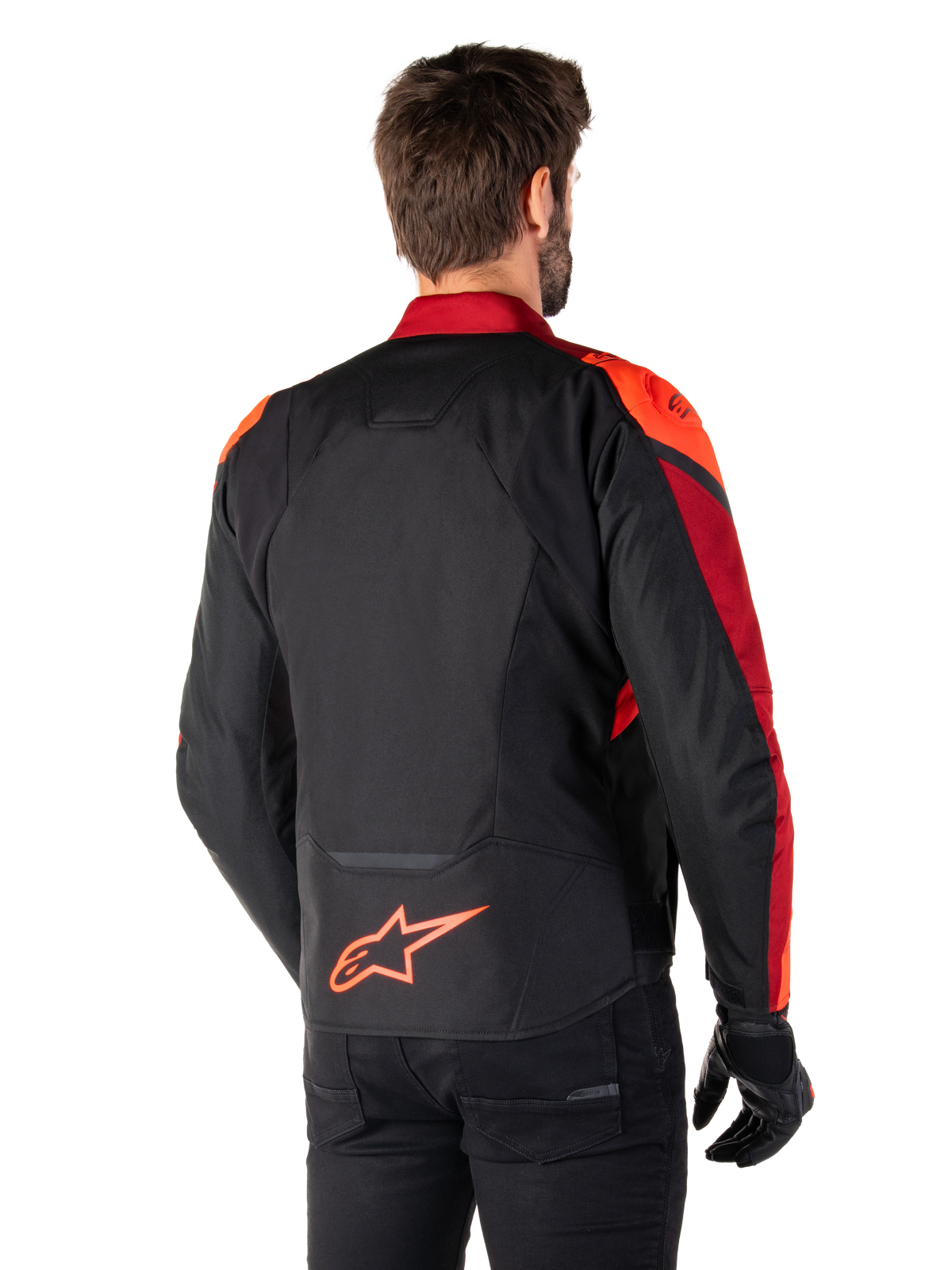 Rückansicht eines Mannes, der die Alpinestars T-Jaws V4 Wasserdichte Jacke in Schwarz Rot Fluo Dunkelrot trägt, mit leuchtend roten Akzenten an den Schultern und Ärmeln, einem fluoreszierend roten Alpinestars-Logo auf dem unteren Rücken, kombiniert mit einer schwarzen Hose und Handschuhen.