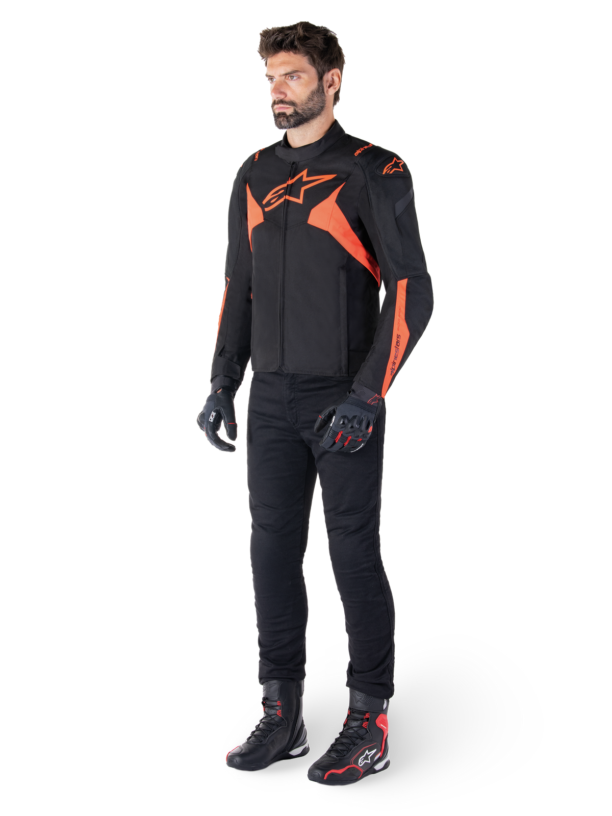 Veste imperméable Alpinestars T-Jaws V4, noir et rouge fluo, portée par un mannequin homme avec pantalon, gants et bottes noirs, avec des accents orange vif et le logo Alpinestars, design sportif pour la conduite de moto