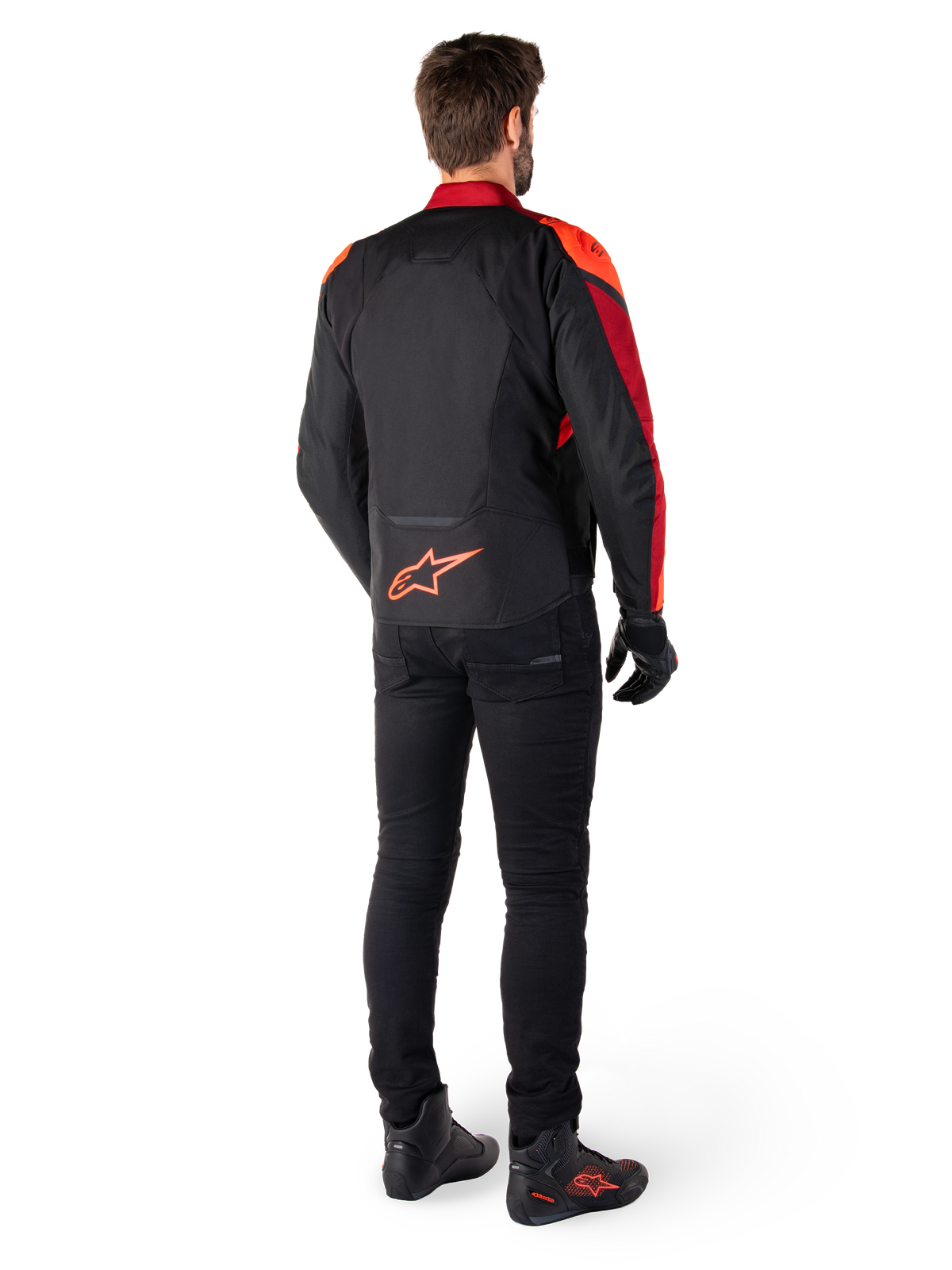 Alpinestars T-Jaws V4 Wasserdichte Jacke in Schwarz Rot Fluo Dunkelrot, Rückansicht eines Fahrers, der die Textiljacke mit schwarzer Hose und Motorradstiefeln trägt, mit einem markanten roten Alpinestars-Logo auf dem unteren Rücken.