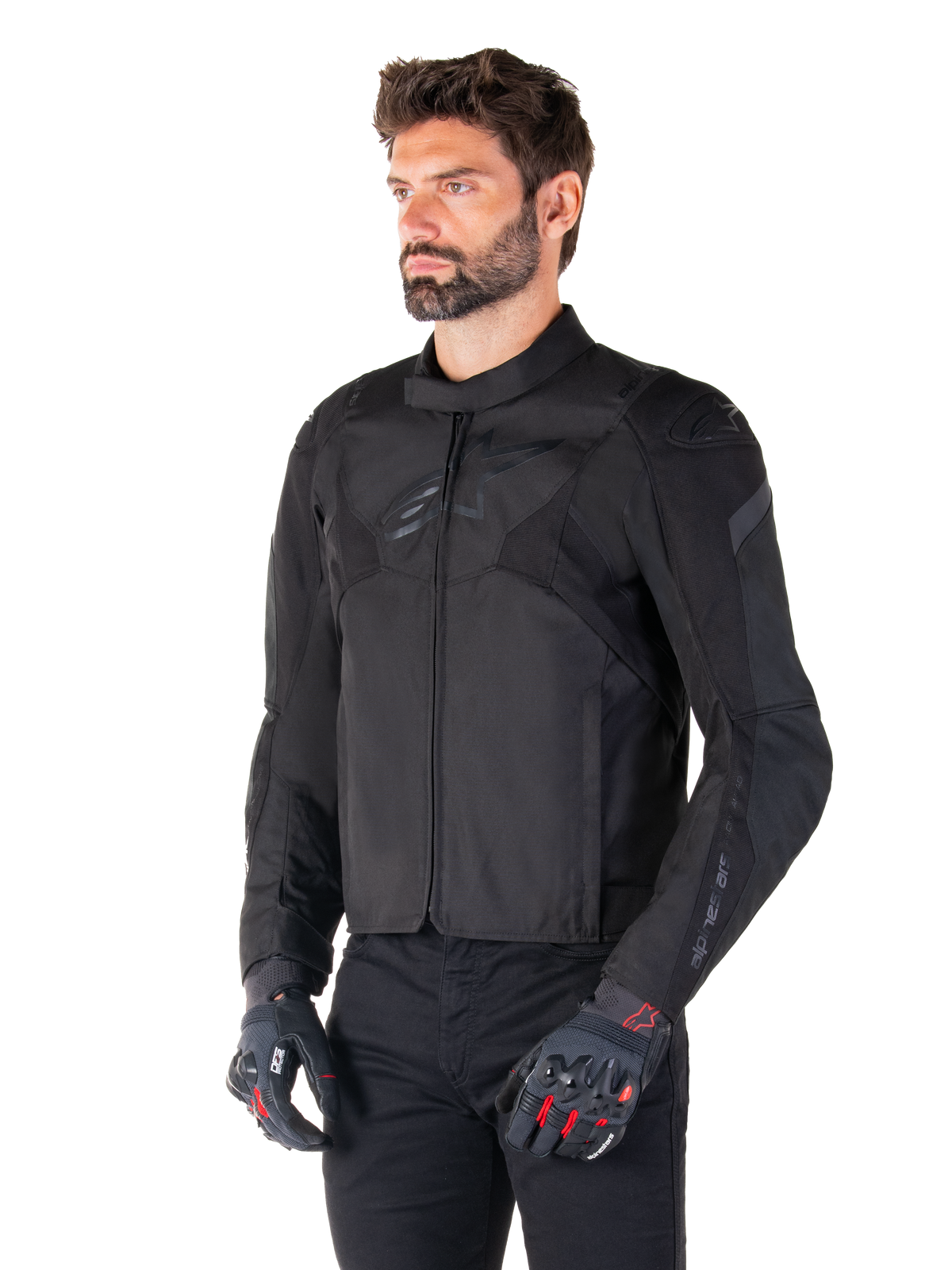 Männlicher Fahrer in der wasserdichten Alpinestars T-Jaws V4 Jacke in Schwarz, kombiniert mit einer schwarzen Hose und Schutzhandschuhen, mit einer schlanken sportlichen Passform, tonalen Alpinestars-Logos auf der Brust und den Schultern sowie einer leistungsstarken Textilkonstruktion.