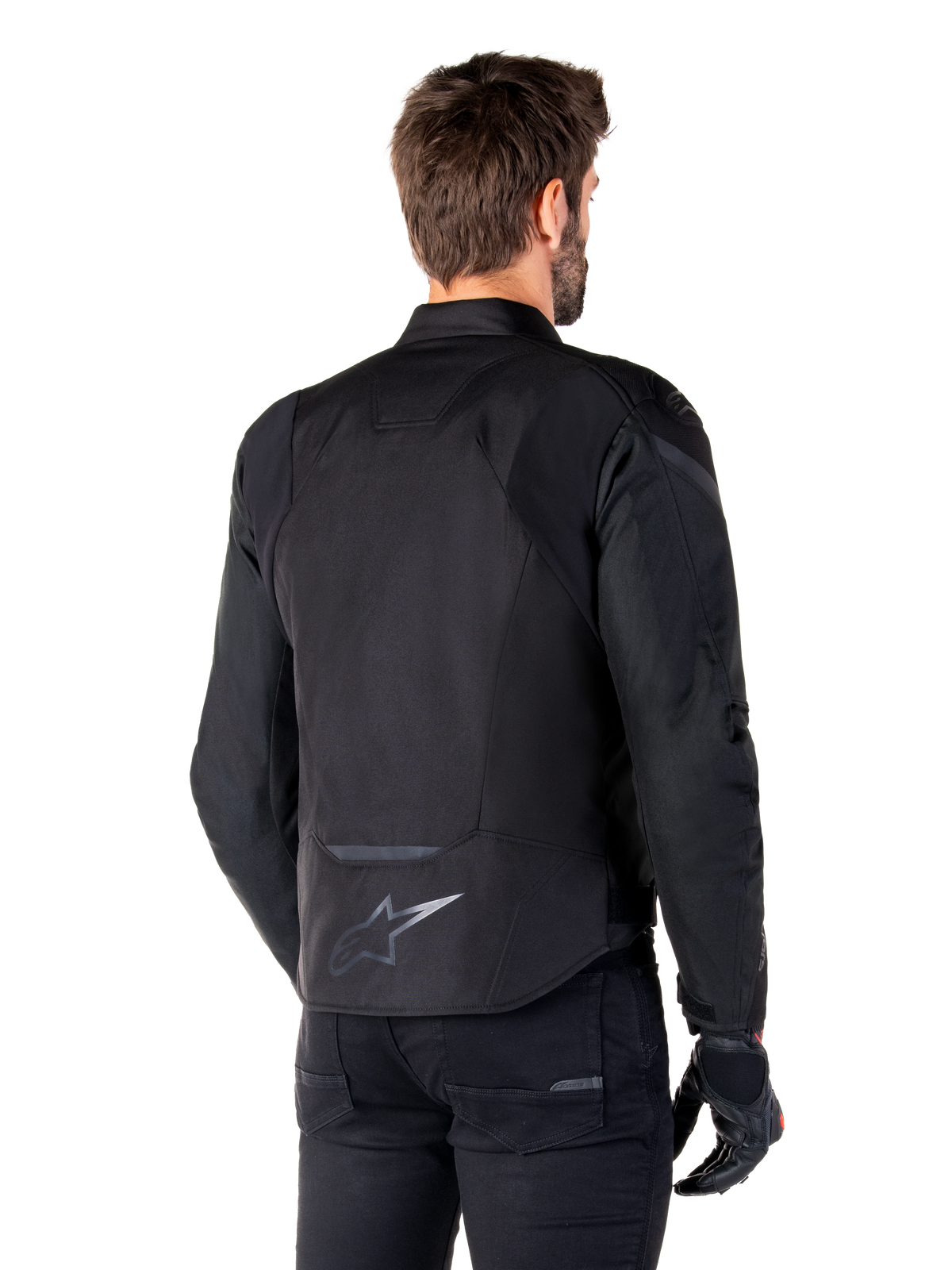 Alpinestars T-Jaws V4 Wasserdichte Jacke, Schwarz, Rückansicht am Modell, mit reflektierendem Alpinestars-Logo am unteren Rücken, verlängerte Rückenpartie für mehr Abdeckung, sportliches Textildesign mit farblich abgestimmten Einsätzen, getragen mit schwarzen Motorradhandschuhen