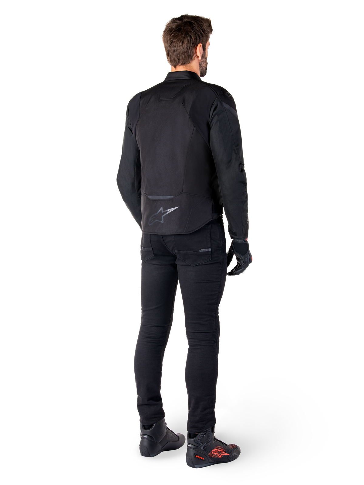 Alpinestars T-Jaws V4 Wasserdichte Jacke, Schwarz, Rückansicht am Modell mit schwarzer Motorradhose und Stiefeln, zeigt die sportliche Textilkonstruktion und das Alpinestars-Logo am unteren Rücken.