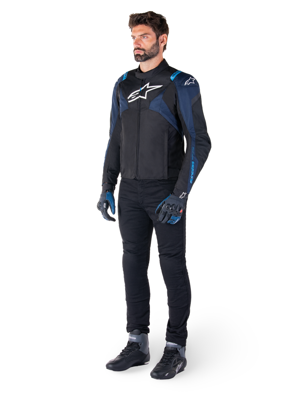 Veste imperméable Alpinestars T-Jaws V4 en noir, bleu foncé et bleu blithe, portée par un mannequin avec un pantalon de moto noir et des bottes de pilotage, avec logo Alpinestars blanc sur la poitrine et accents bleus aux épaules, équipement de moto coupe sport.