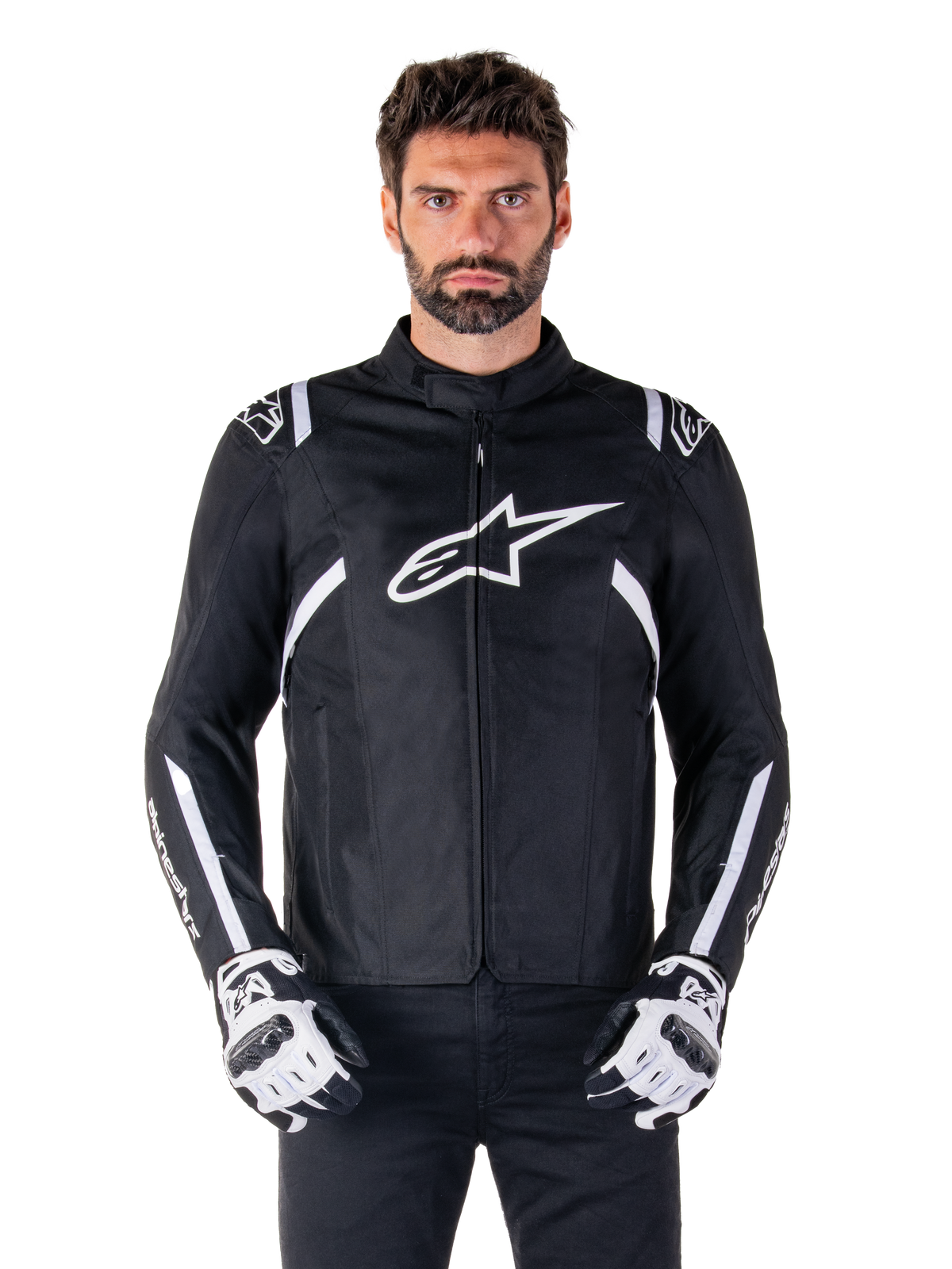 Alpinestars T-SPS V2 Waterproof Jacket in zwart en wit, vooraanzicht op model, waterdichte textiele motorjas met witte schouder- en armstrepen, groot wit Alpinestars-logo op de borst, gedragen met beschermende motorhandschoenen, strak sportief silhouet