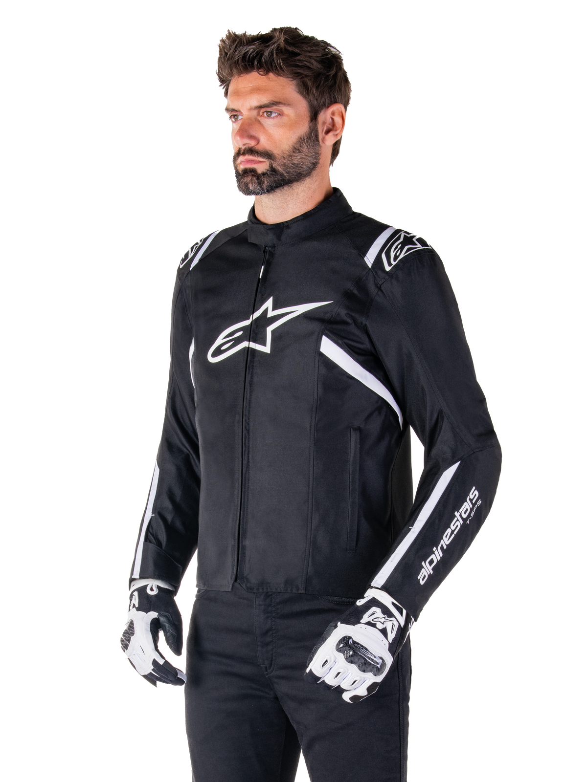 Alpinestars T-SPS V2 Waterproof Jas, zwart en wit, gedragen door mannelijk model met bijpassende motorhandschoenen, sportief gesneden textieljas met witte Alpinestars-logo's op de borst en schouders, 'alpinestars T-SPS' branding op de mouw, strakke op races geïnspireerde motoruitrusting