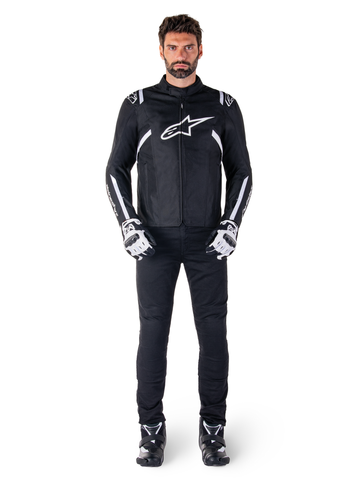 Alpinestars T-SPS V2 Waterproof jas, zwart en wit, gedragen door mannelijk model met zwarte broek en bijpassende handschoenen, voorzien van wit Alpinestars-logo op de borst en accenten op de mouwen, sportieve pasvorm voor motorrijden in alle weersomstandigheden