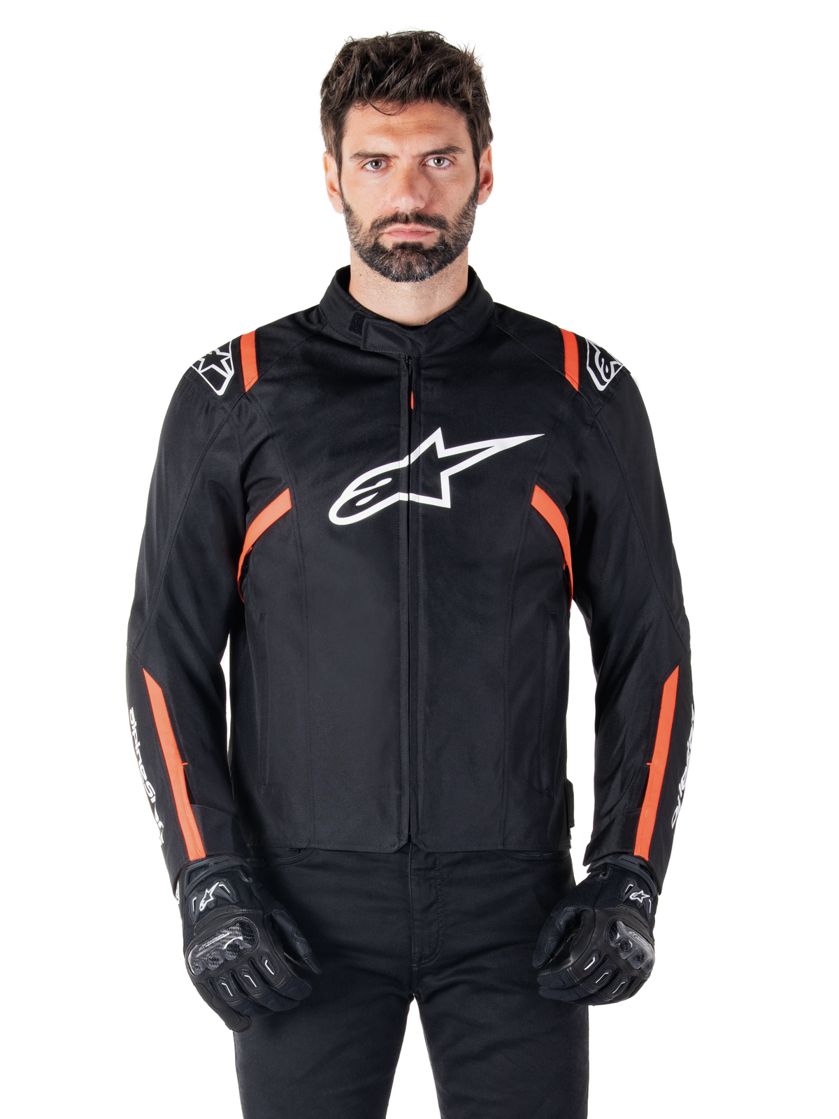 Alpinestars T-SPS V2 Wasserdichte Jacke, Schwarz, Weiß und Leuchtrot, getragen von einem männlichen Model mit schwarzen Motorradhandschuhen, mit einem großen weißen Alpinestars-Logo auf der Brust und leuchtend orangefarbenen Akzenten an den Schultern und Ärmeln.