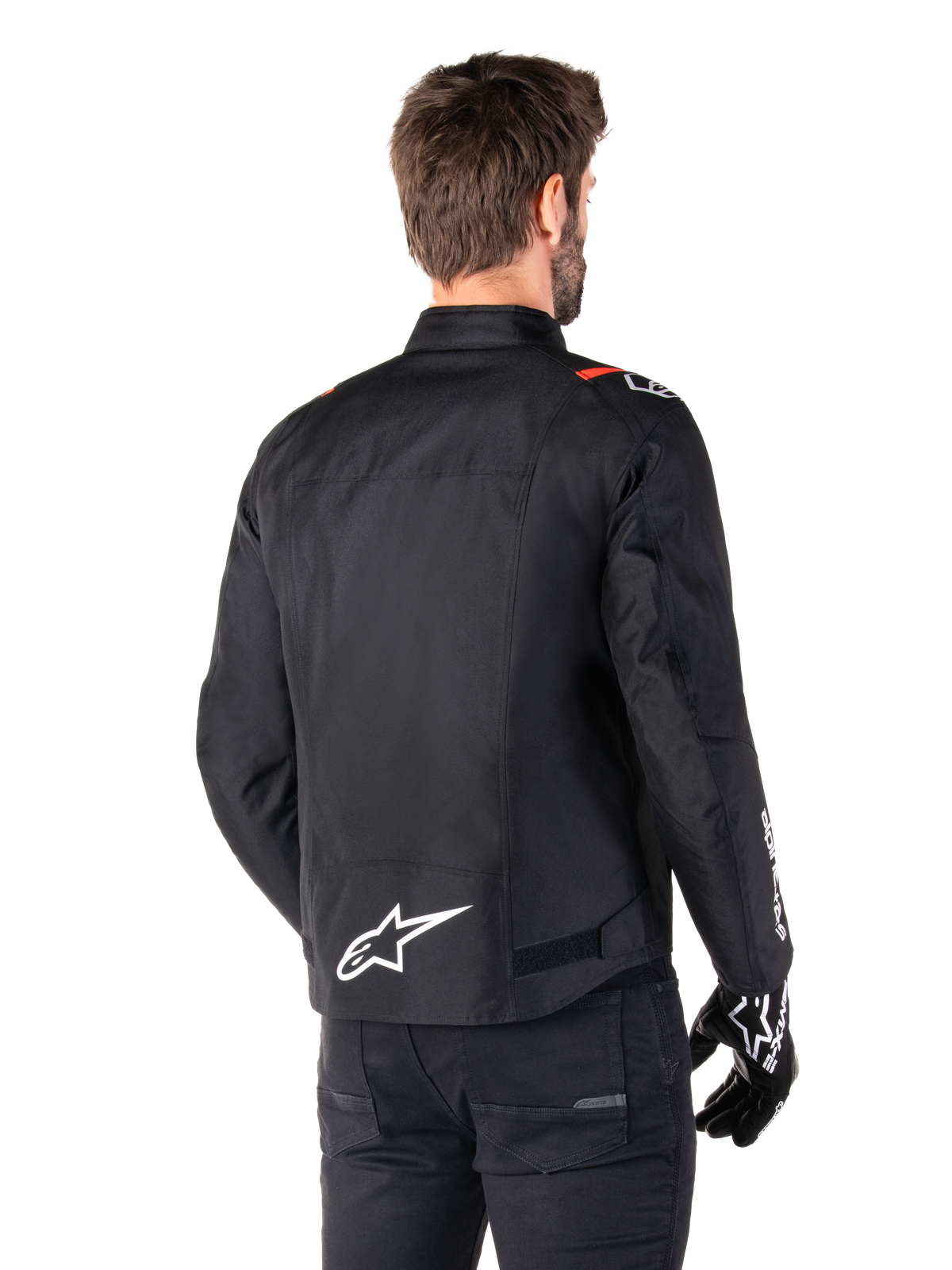 Alpinestars T-SPS V2 Wasserdichte Jacke, Schwarz Weiß Rot Fluo, Rückansicht, mit weißem Alpinestars-Logo am unteren Rücken und roten Akzenten an den Schultern, getragen mit schwarzen Motorradhandschuhen und -hosen, Textil-Motorradjacke im Sport-Stil
