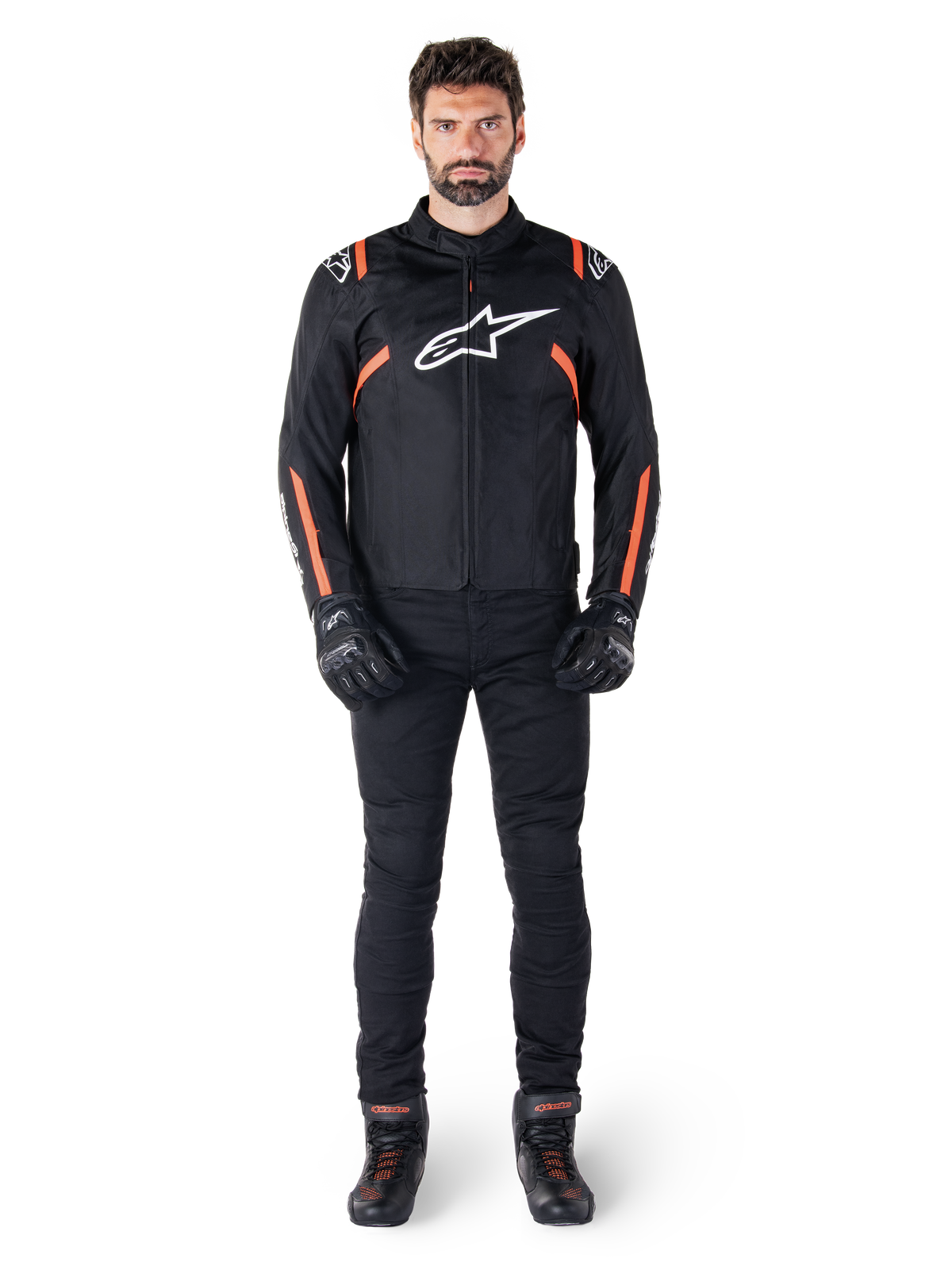 Männliches Model trägt die Alpinestars T-SPS V2 Waterproof Jacke in Schwarz Weiß Rot Fluo, kombiniert mit schwarzer Motorradhose und Handschuhen, mit einem weißen Alpinestars-Logo auf der Brust und roten Akzenten an den Ärmeln.