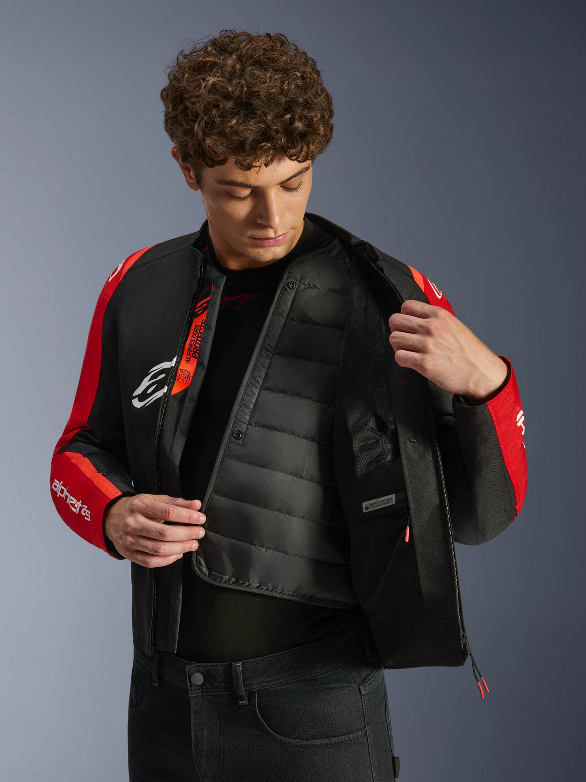 Alpinestars T-SPS V2 Waterproof Jacket, Black and Red, featuring a model revealing the internal quilted thermal liner and waterproof compartment, Tech-Air Ready branding on the interior, sport-cut motorcycle jacket.